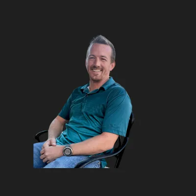 Smiling man sitting on an office chair wearing a blue polo shirt and jeans, isolated on black background