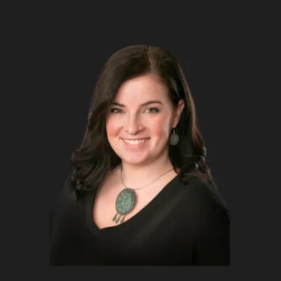 Smiling woman with dark hair wearing black top and turquoise jewelry against a dark background