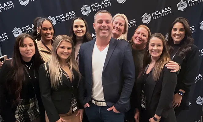 Group of diverse professionals at a real estate event posing in front of a 