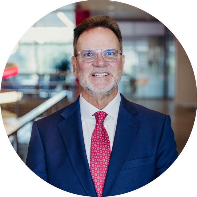 Professional man in a business suit smiling, indoor office environment with modern decor, colorful lighting, and glass walls.