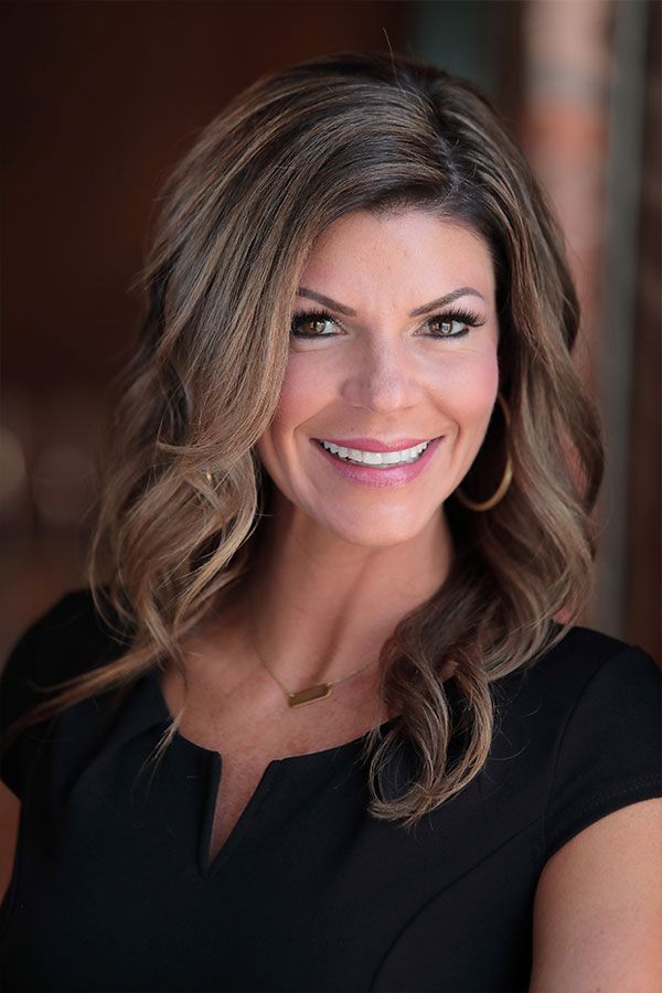 Smiling woman with blonde hair in a white shirt standing outdoors among tall grass.