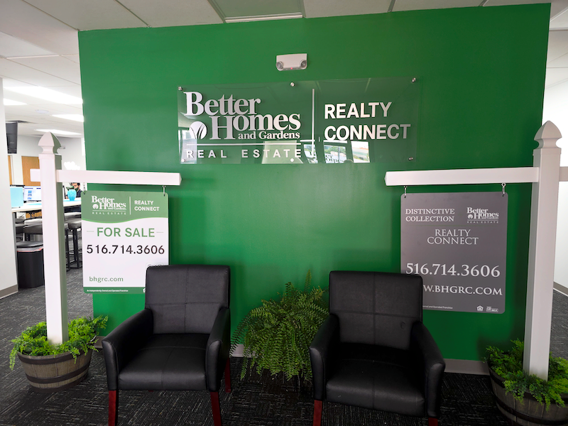 Reception area of Realty Connect USA real estate office with a wooden front desk, blue accent wall, and company logo