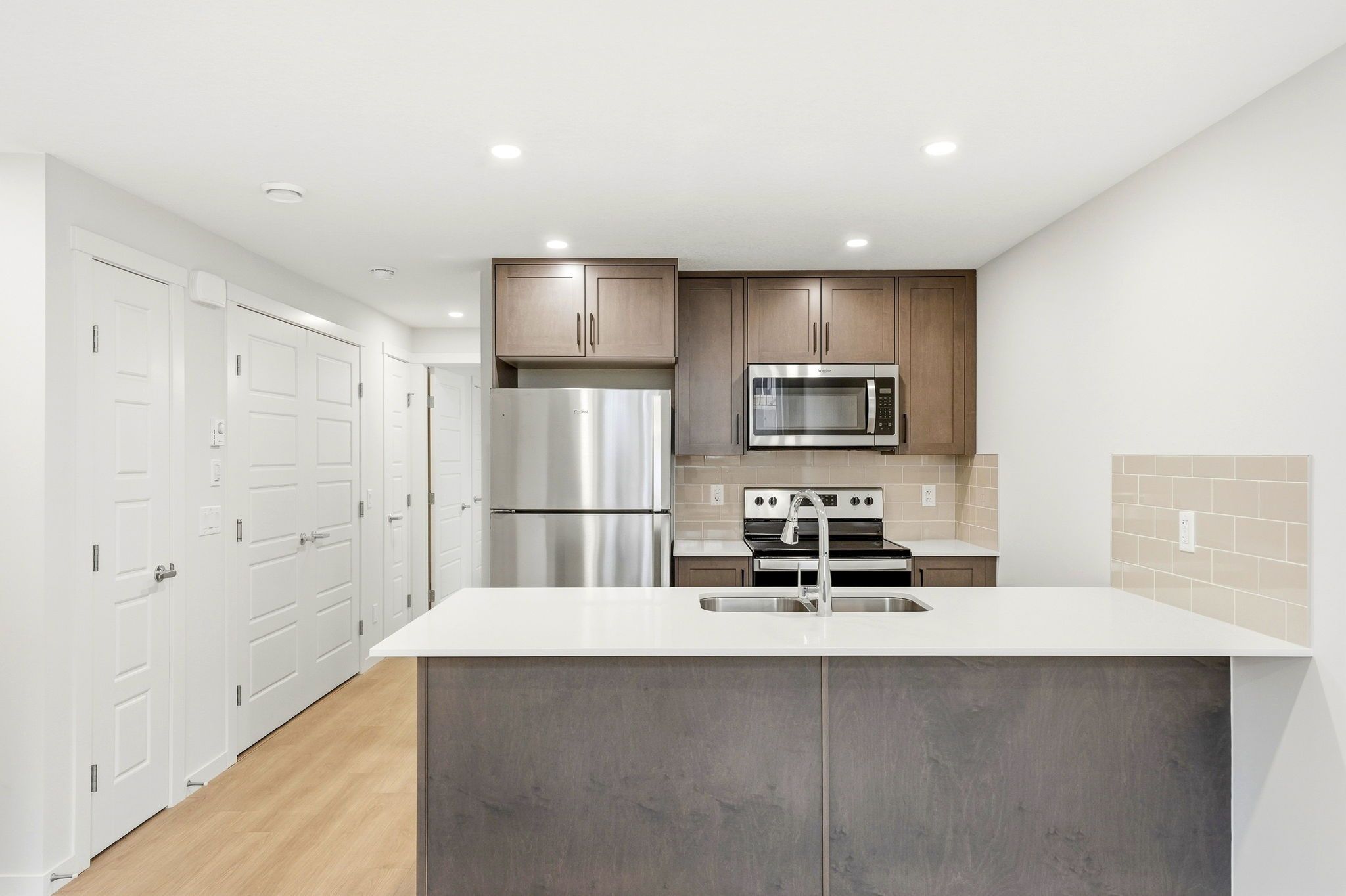 Kitchen with quartz peninsula, breakfast bar and stainless appliances in the identical neighbouring Braeburn unit at ZEN Livingston, Calgary