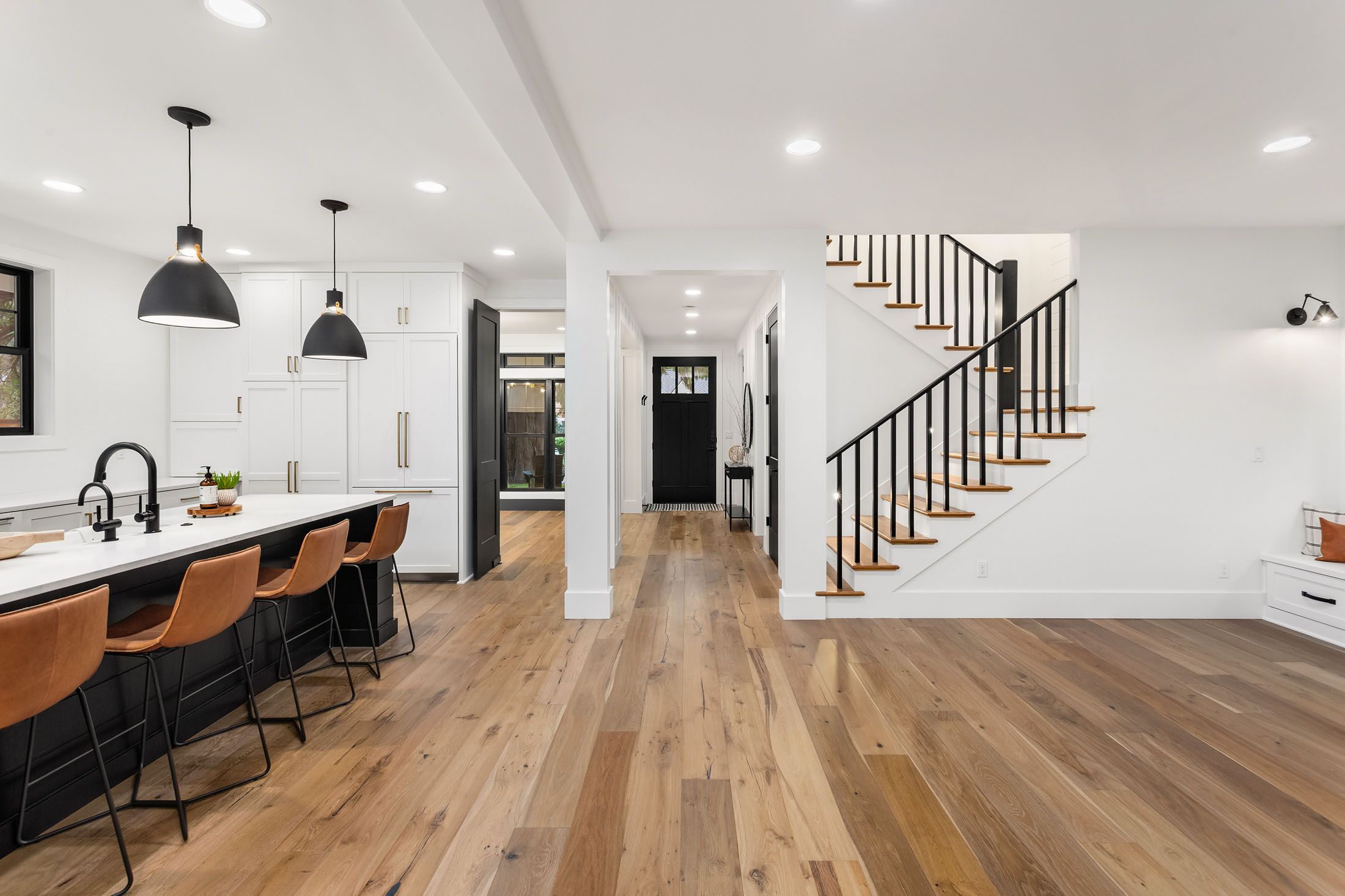 Modern open-concept kitchen and living room with white walls, black accents, wooden flooring, and a staircase with black railings
