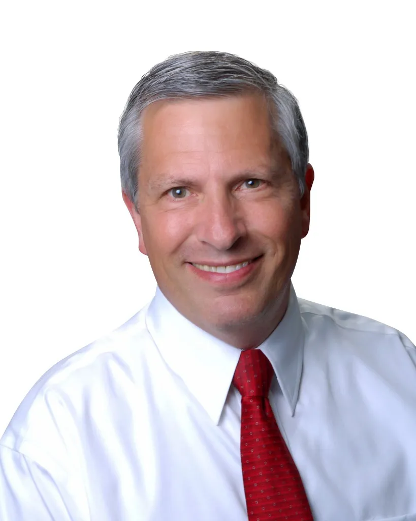 Smiling man with short brown hair wearing a multicolored checkered shirt in a professional portrait against a white background