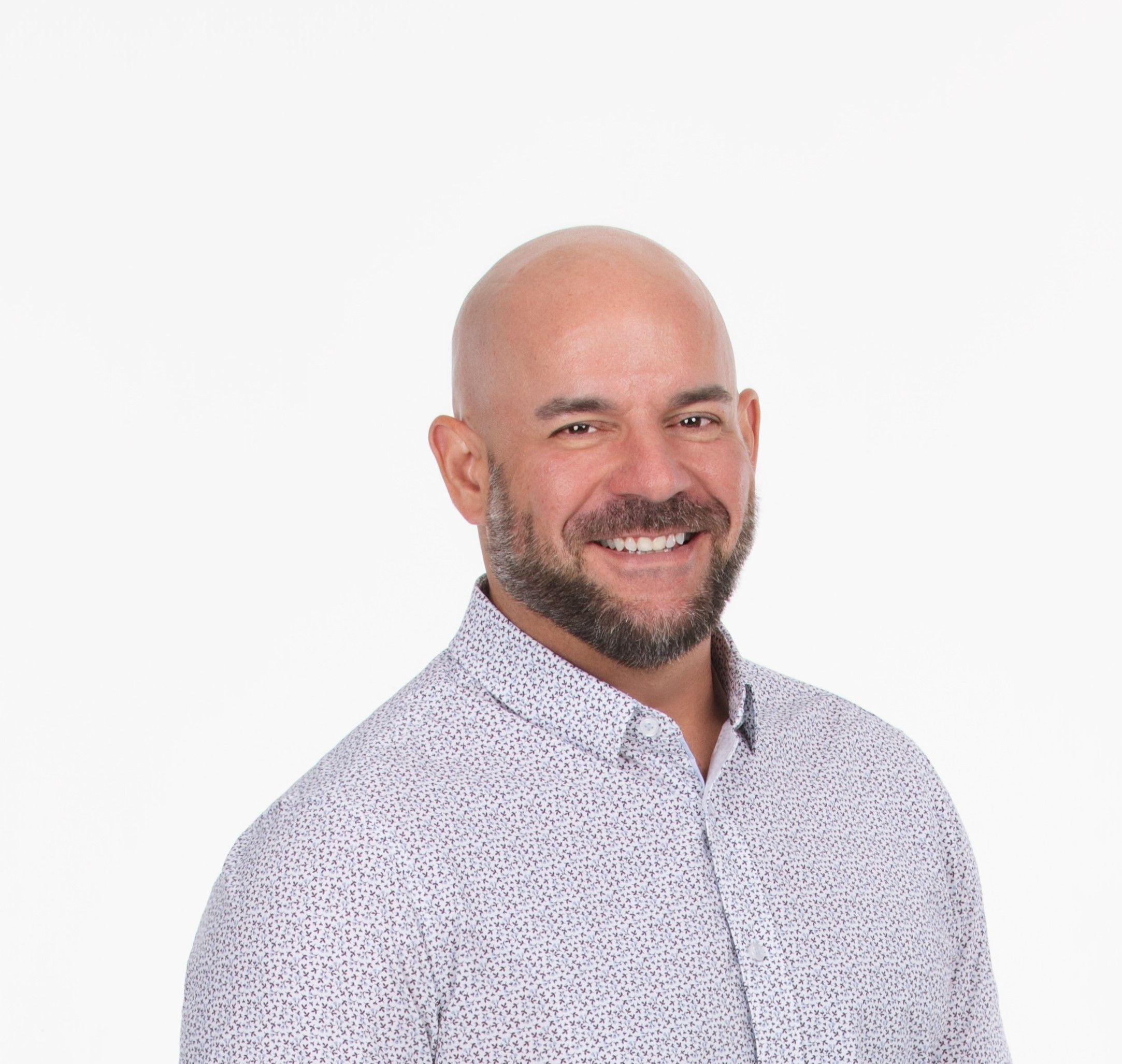 Professional headshot of a smiling bald man with a beard, wearing a dark suit and white shirt, against a white background.