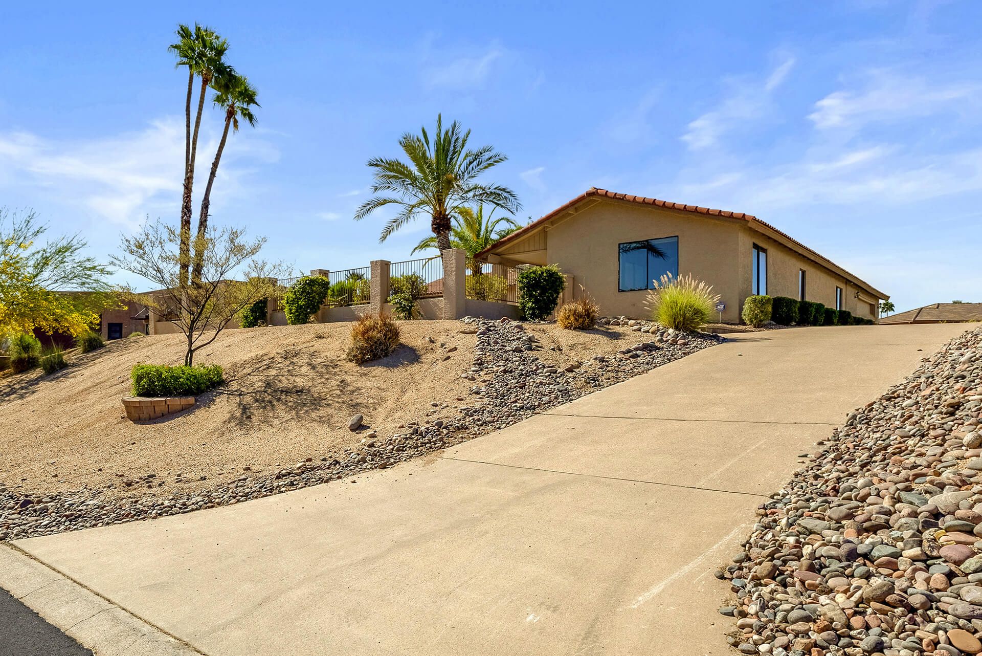 Modern two-story house with beige exterior, attached garage, landscaped front yard, large shade tree, and clear blue sky.
