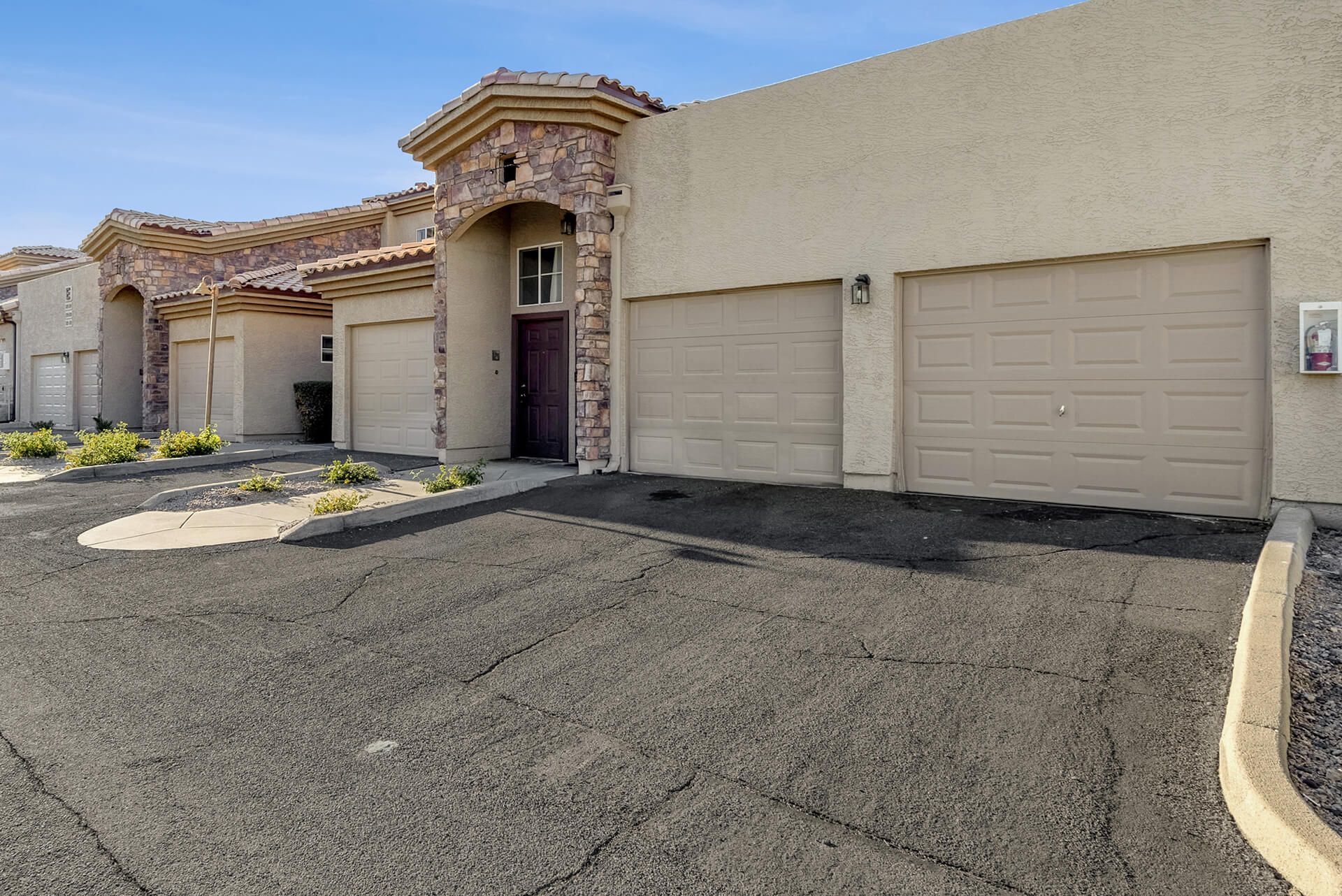 Modern two-story house with beige exterior, attached garage, landscaped front yard, large shade tree, and clear blue sky.