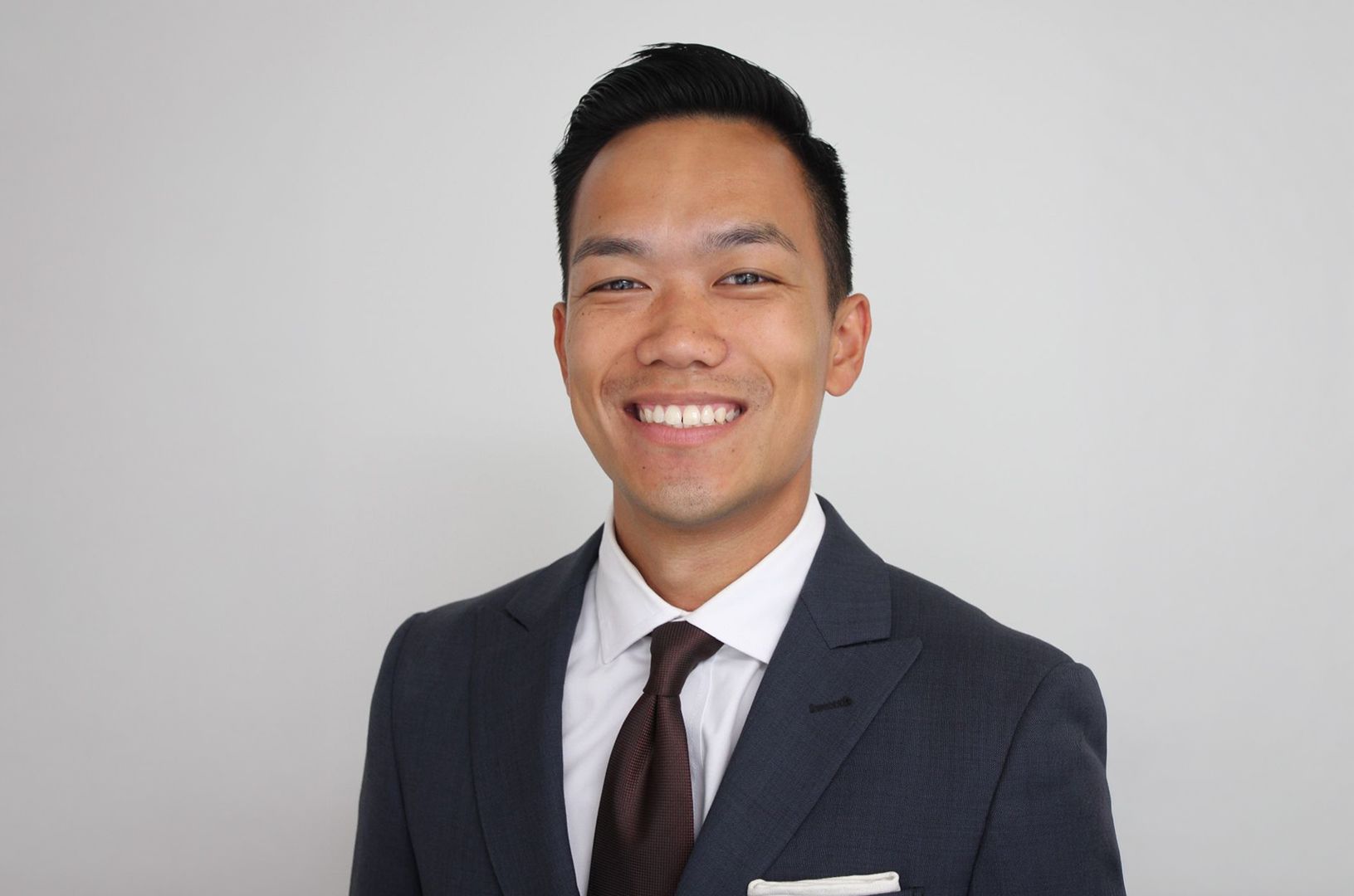 Portrait of a young woman with long brown hair, light skin, blue eyes, wearing a black top, against a light blue background.
