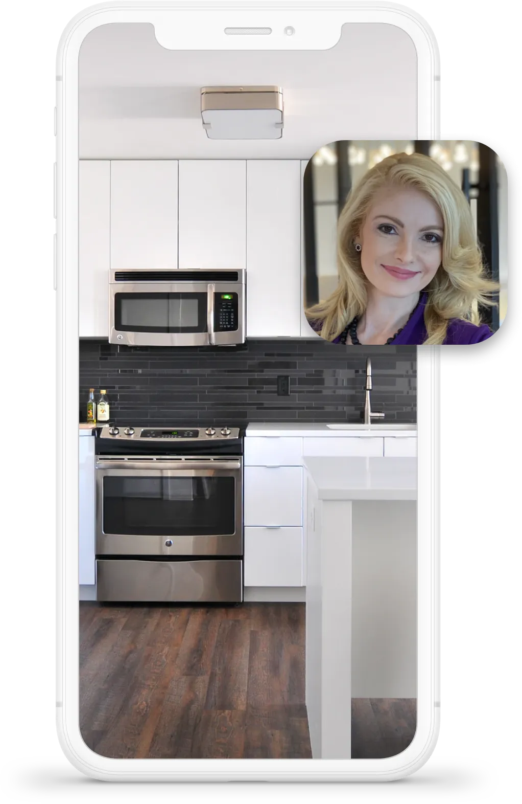 Video call screenshot showing a woman with blonde hair and a purple top in a modern kitchen with white cabinets, black backsplash, and stainless steel appliances.