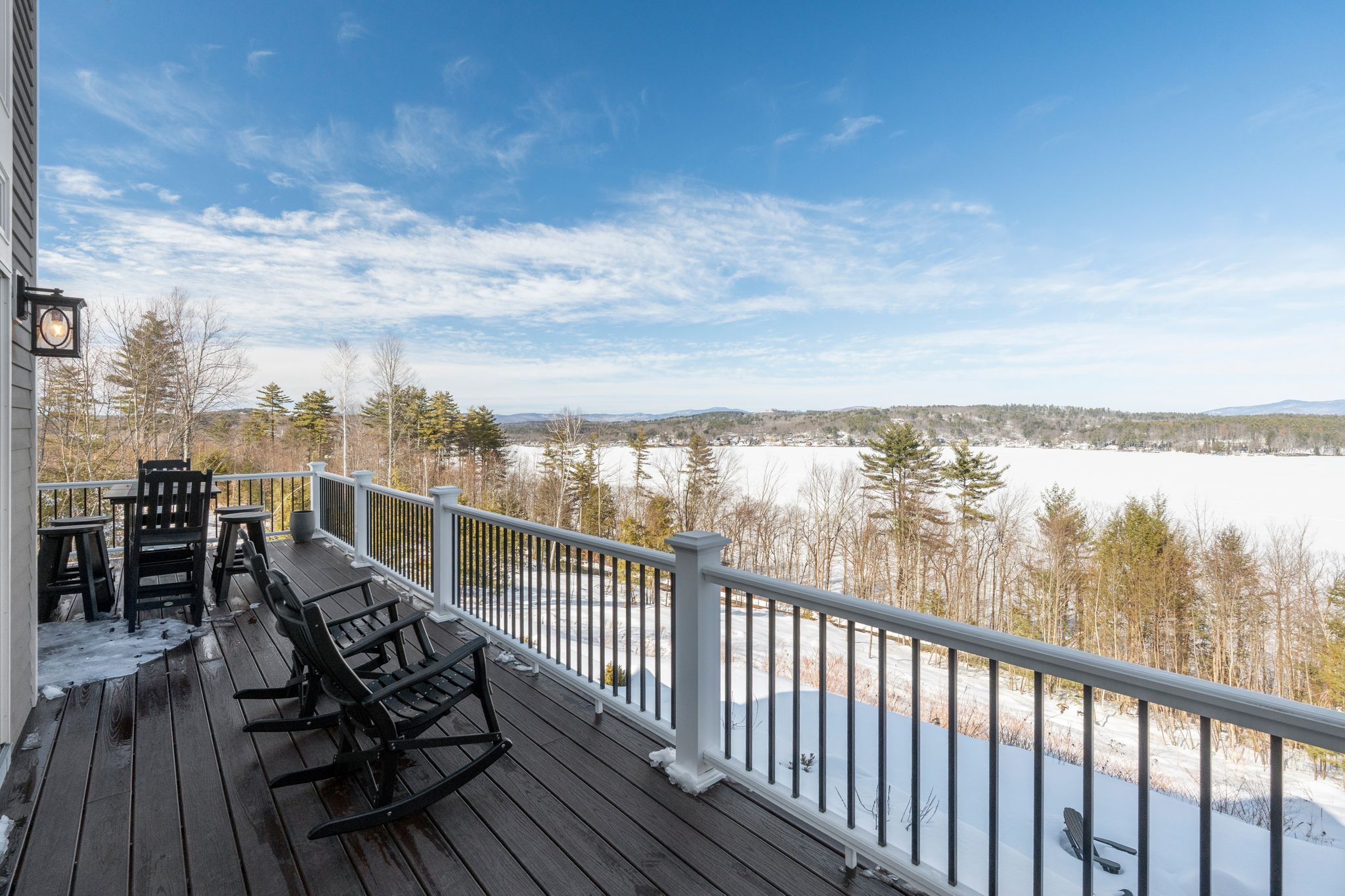 Scenic backyard with a two-story house, lush green lawn, mature trees, a raised porch with an American flag, and a basketball hoop in a wooded area.