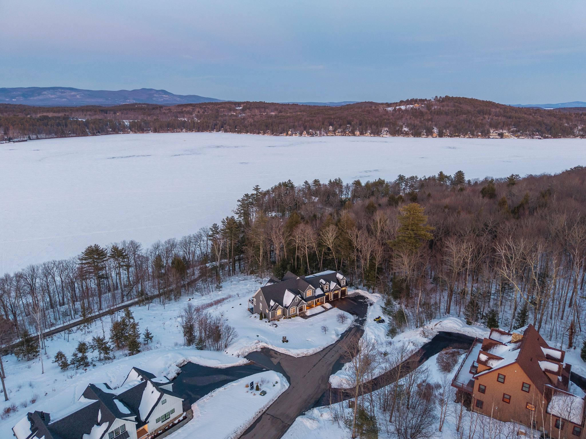 Outdoor backyard patio with a fire pit, Adirondack chairs, and a modern house with a deck and spiral staircase at sunset