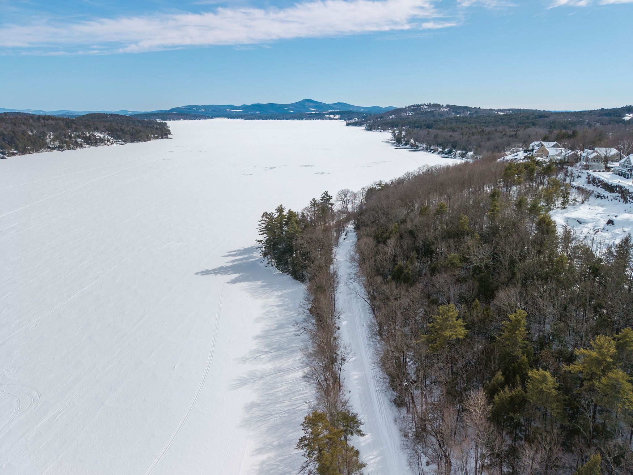Outdoor balcony with two white lounge chairs, a small round table with drinks, overlooking a lush green forest and distant mountains under a partly cloudy sky.