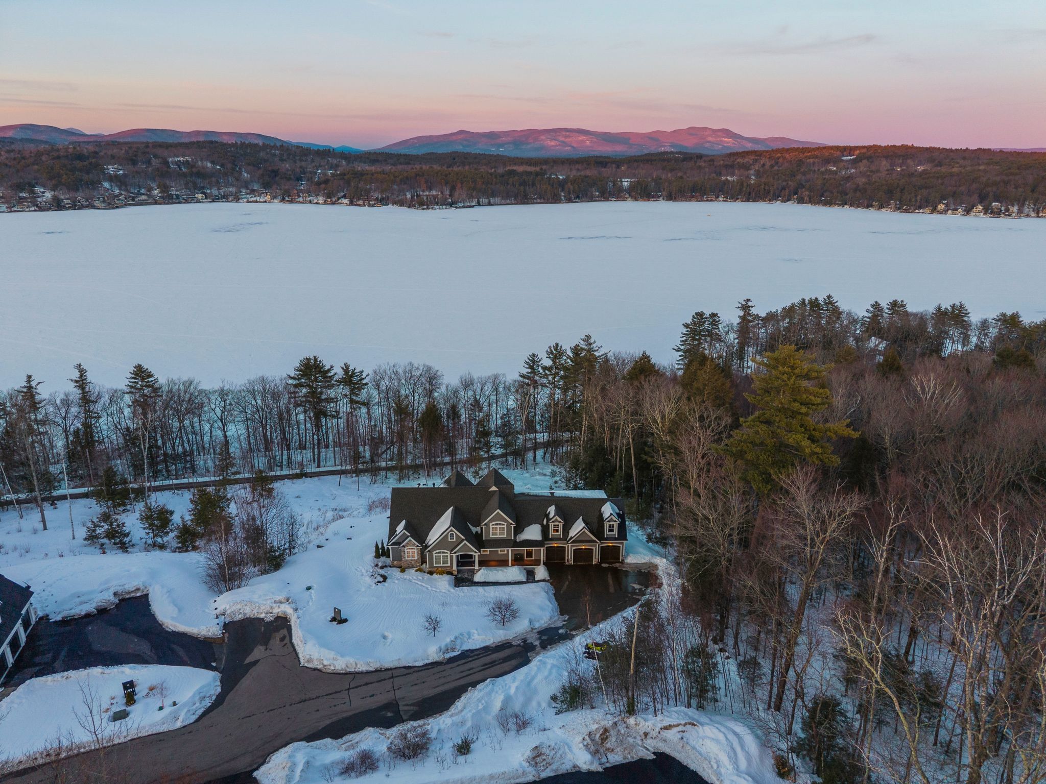 Outdoor kitchen area with stainless steel grill and seating, surrounded by a stone patio, lush green trees, and a black metal fence in the backyard.