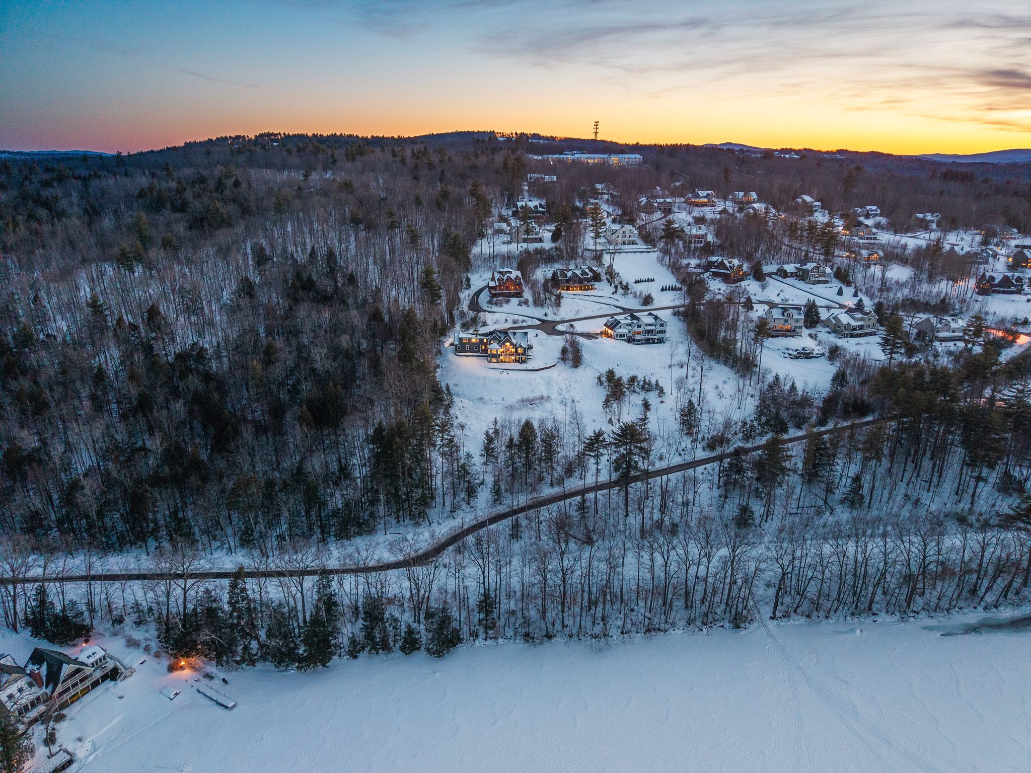 Wooden outdoor playhouse with a green slide in a backyard playground surrounded by black safety fence and lush green trees