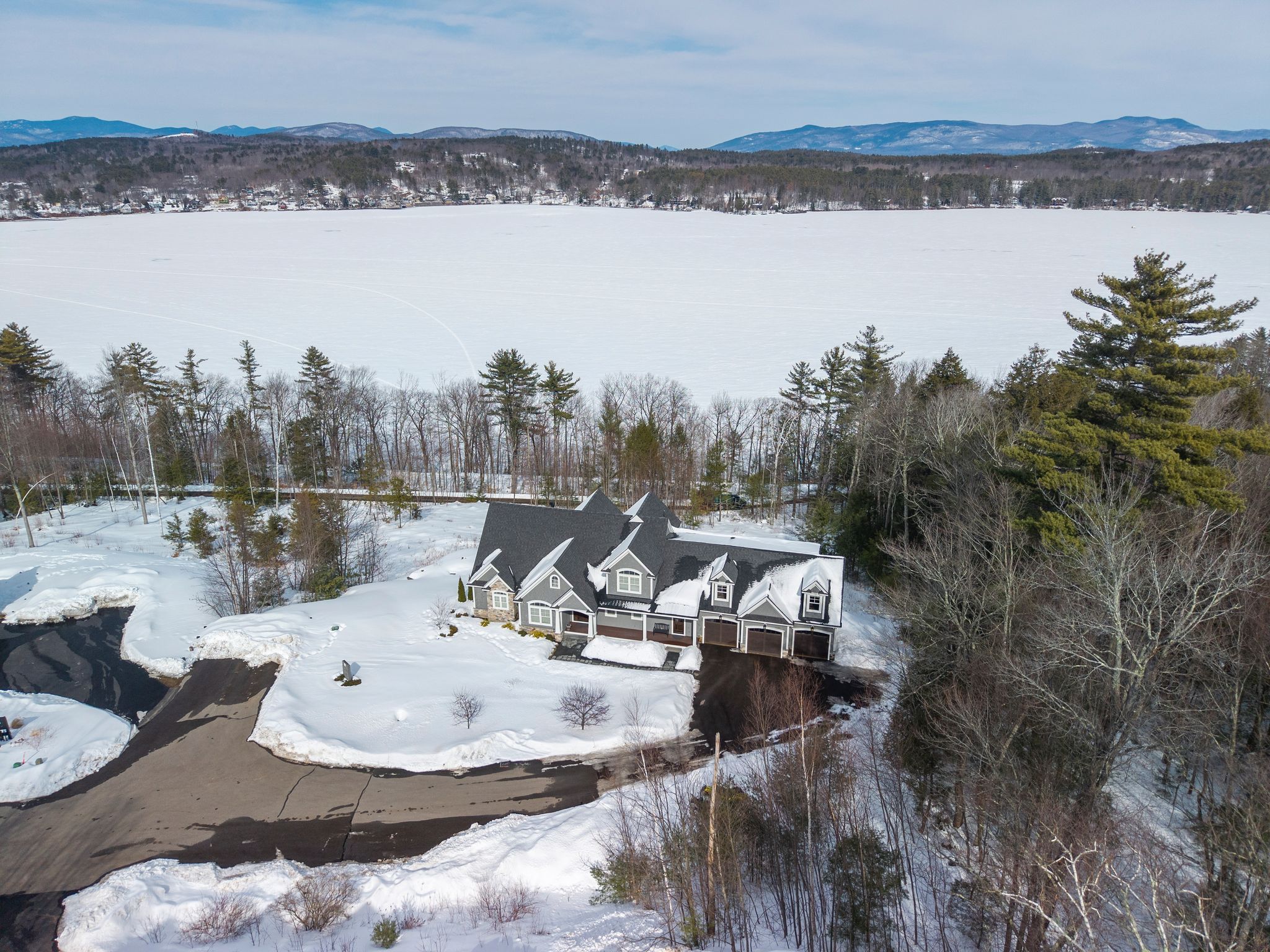 Scenic aerial view of a suburban neighborhood surrounded by lush green forest and rolling hills at sunset.