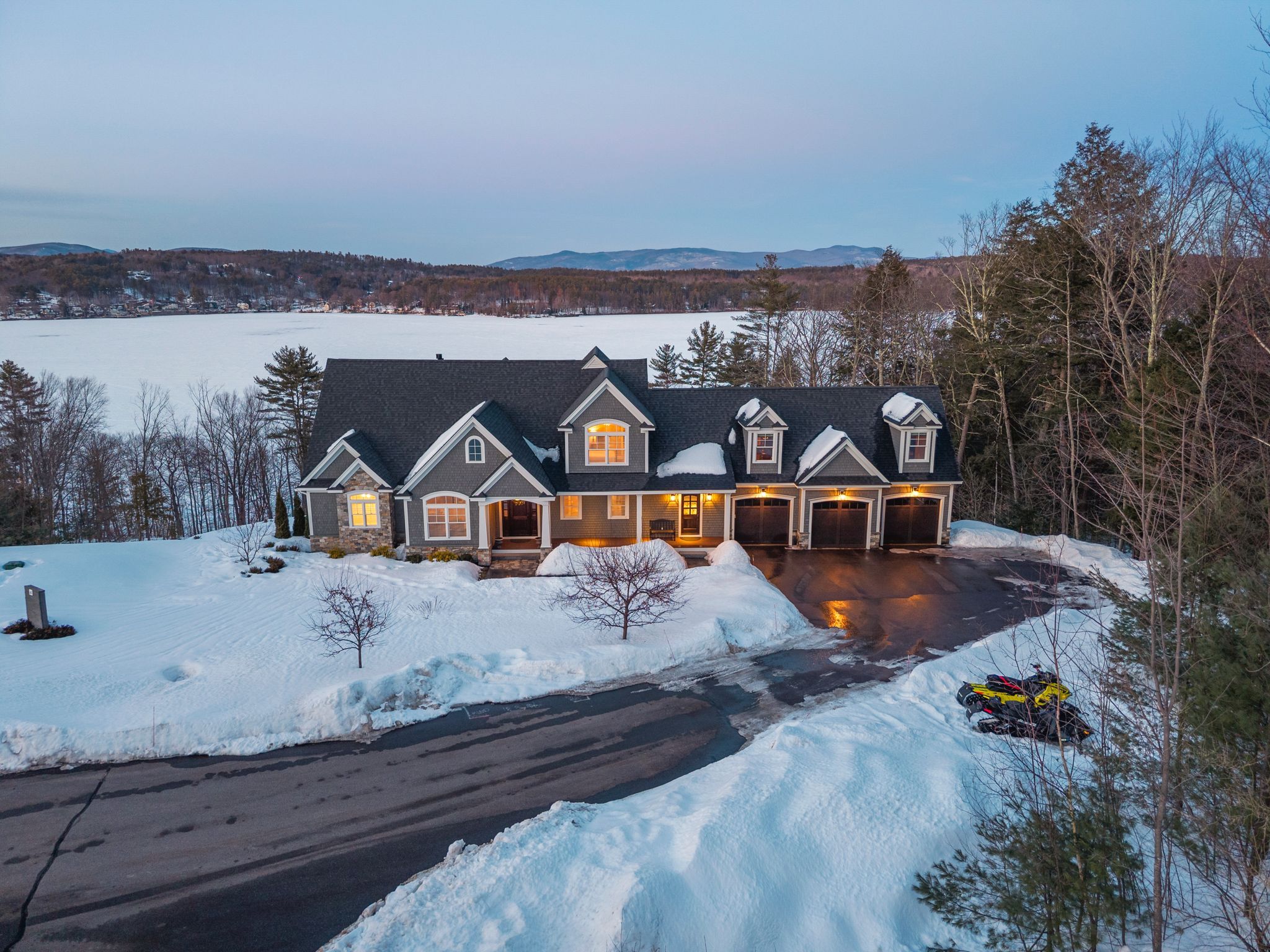 Elegant suburban house at dusk with illuminated windows, a three-car garage, and well-maintained front yard featuring potted plants and pathway lighting.