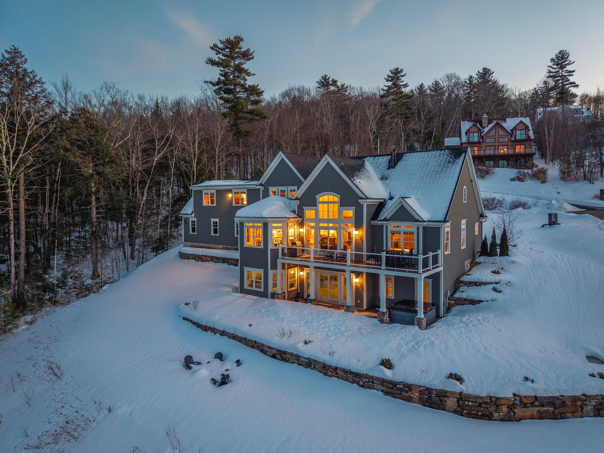 Spacious modern house with large deck overlooking lush green backyard surrounded by trees, under a partly cloudy sky.