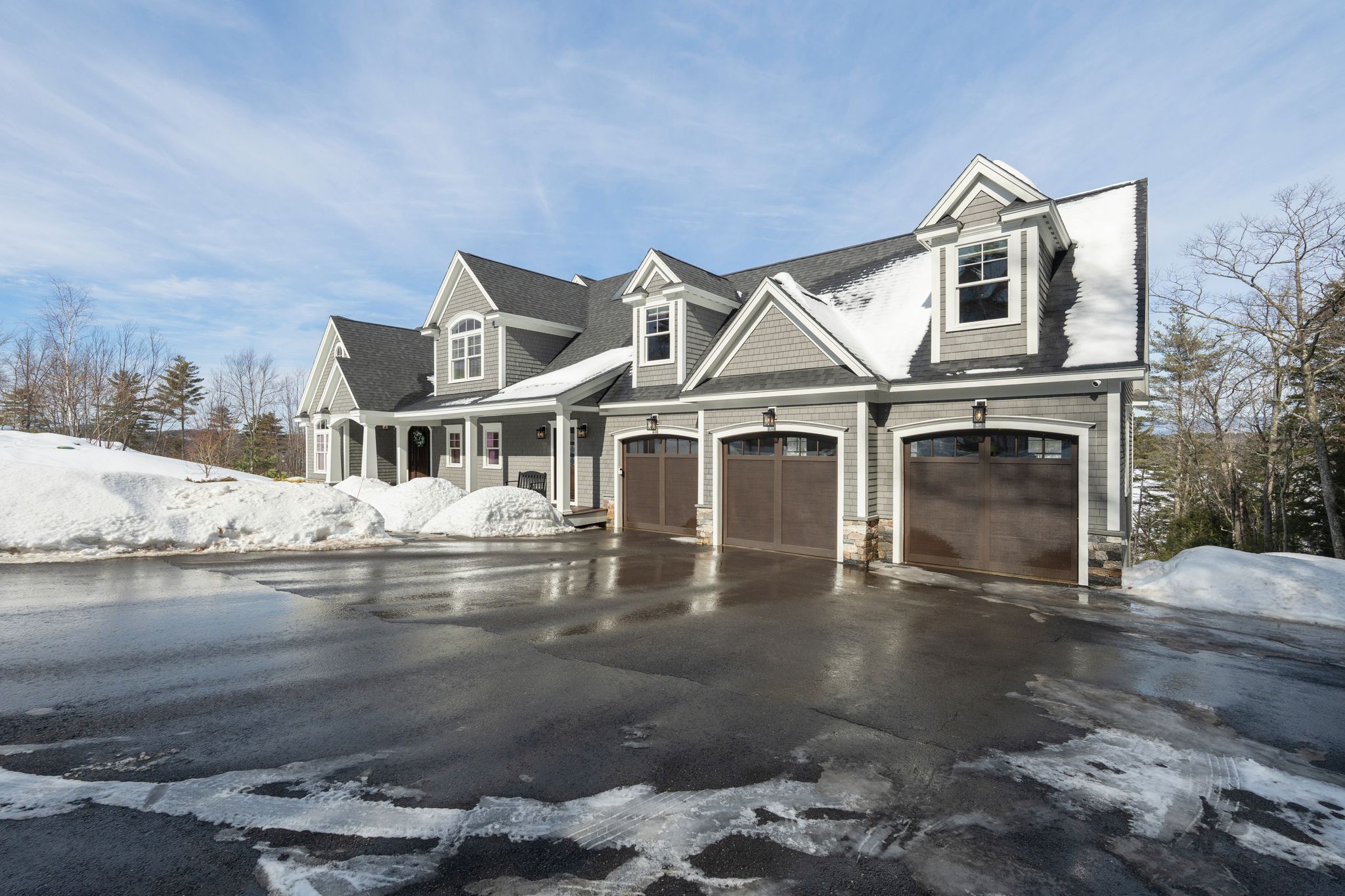 Aerial view of a lush green suburban neighborhood surrounded by dense trees, with a large lake and rolling hills in the background under a partly cloudy sky.