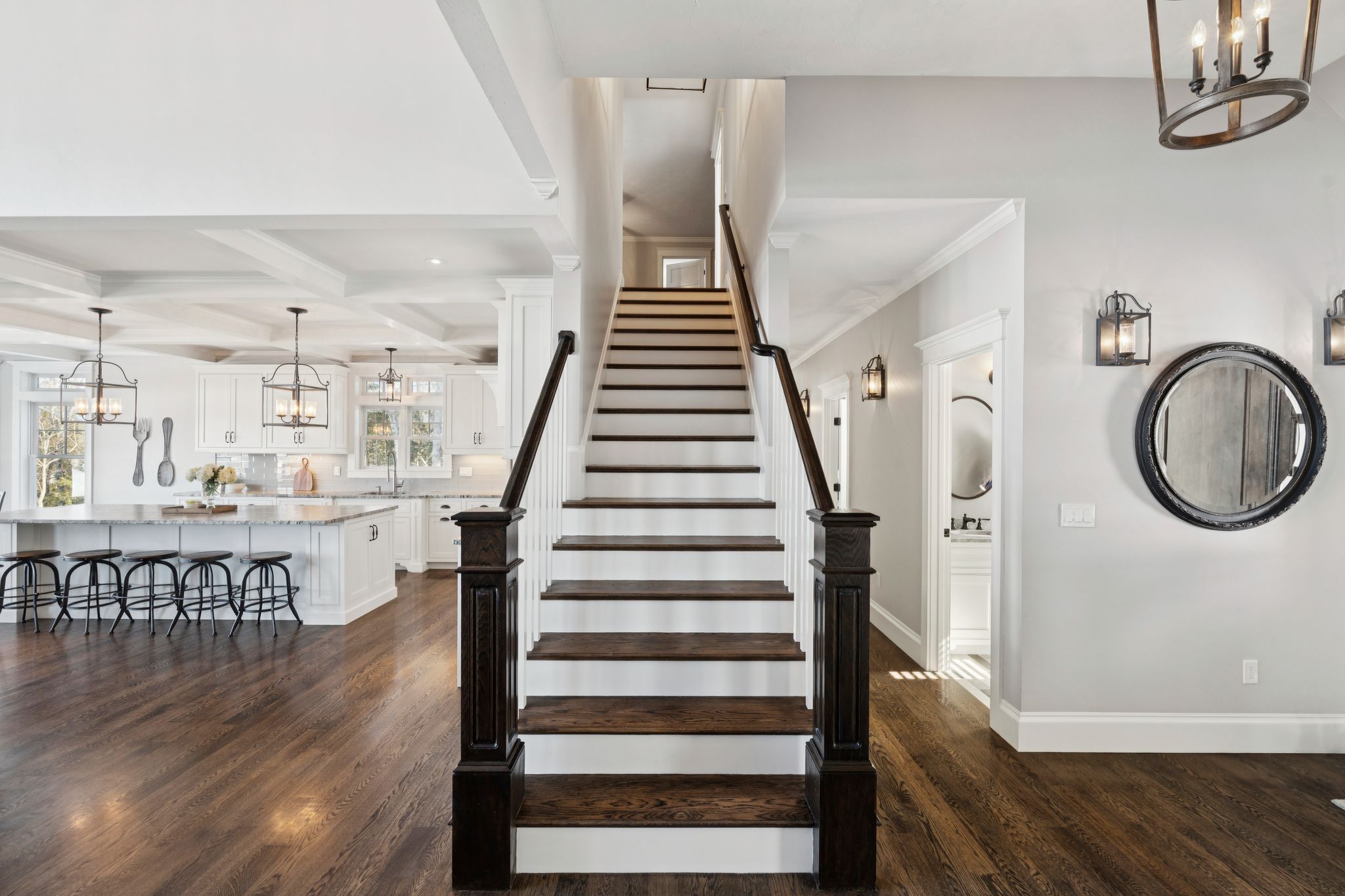 Interior view of a modern home with a built-in wooden bench with blue pillows, a wooden cabinet, framed artwork, and a dining area with large windows showing greenery outside