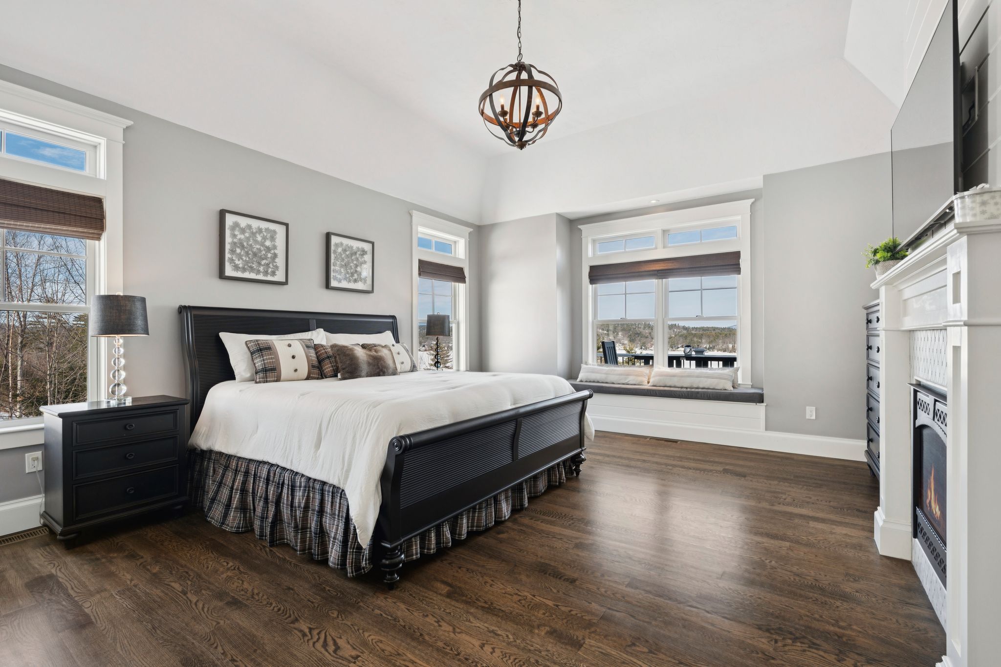 Bright and spacious bedroom with a four-poster bed, large windows with lush greenery view, flat-screen TV, and cozy seating area, featuring a neutral color palette and modern decor.