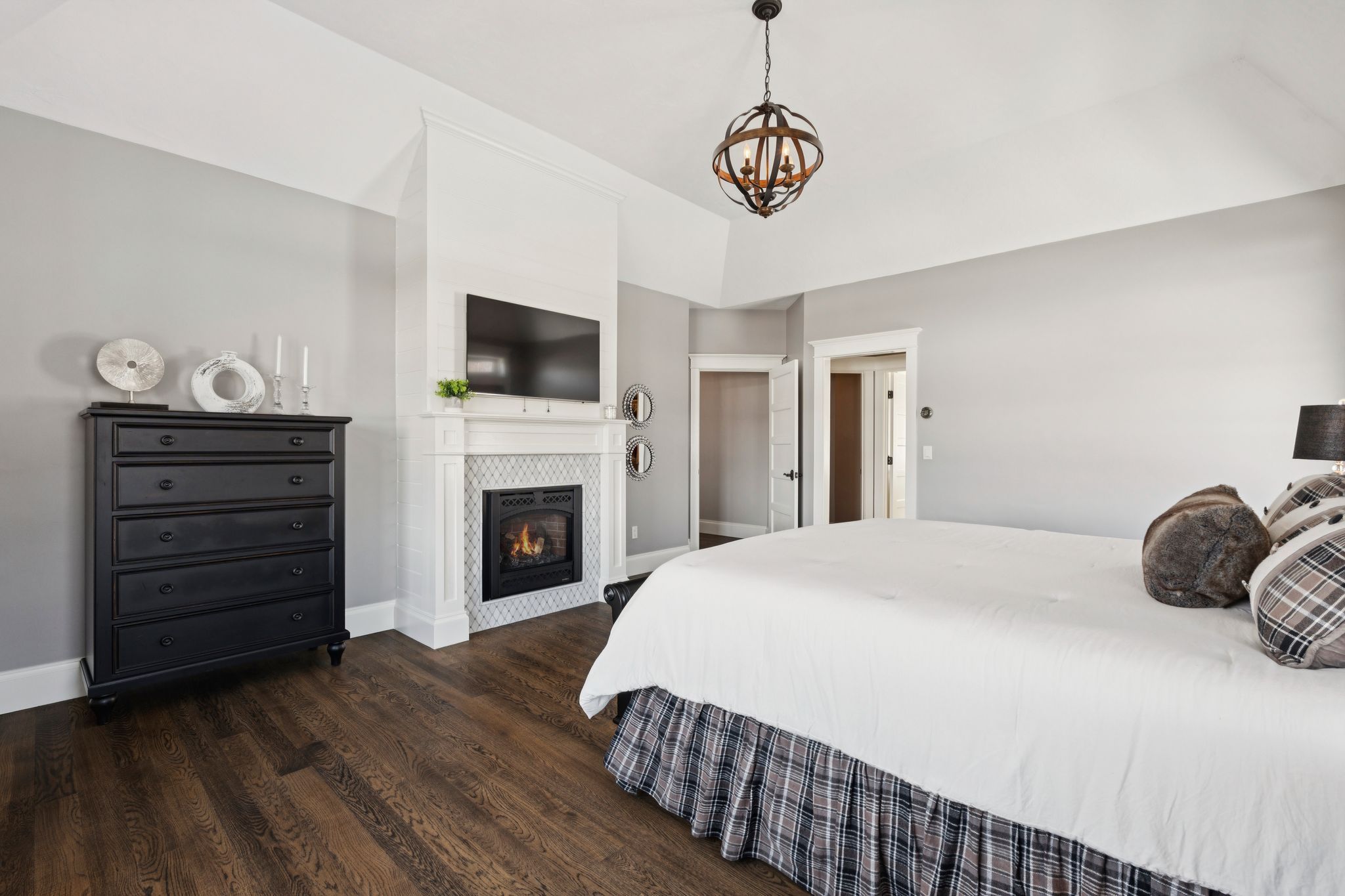 Bright bedroom with a wooden four-poster bed, large windows with white curtains, a ceiling fan, and modern decor including a wall-mounted flat-screen TV and a small sitting area.