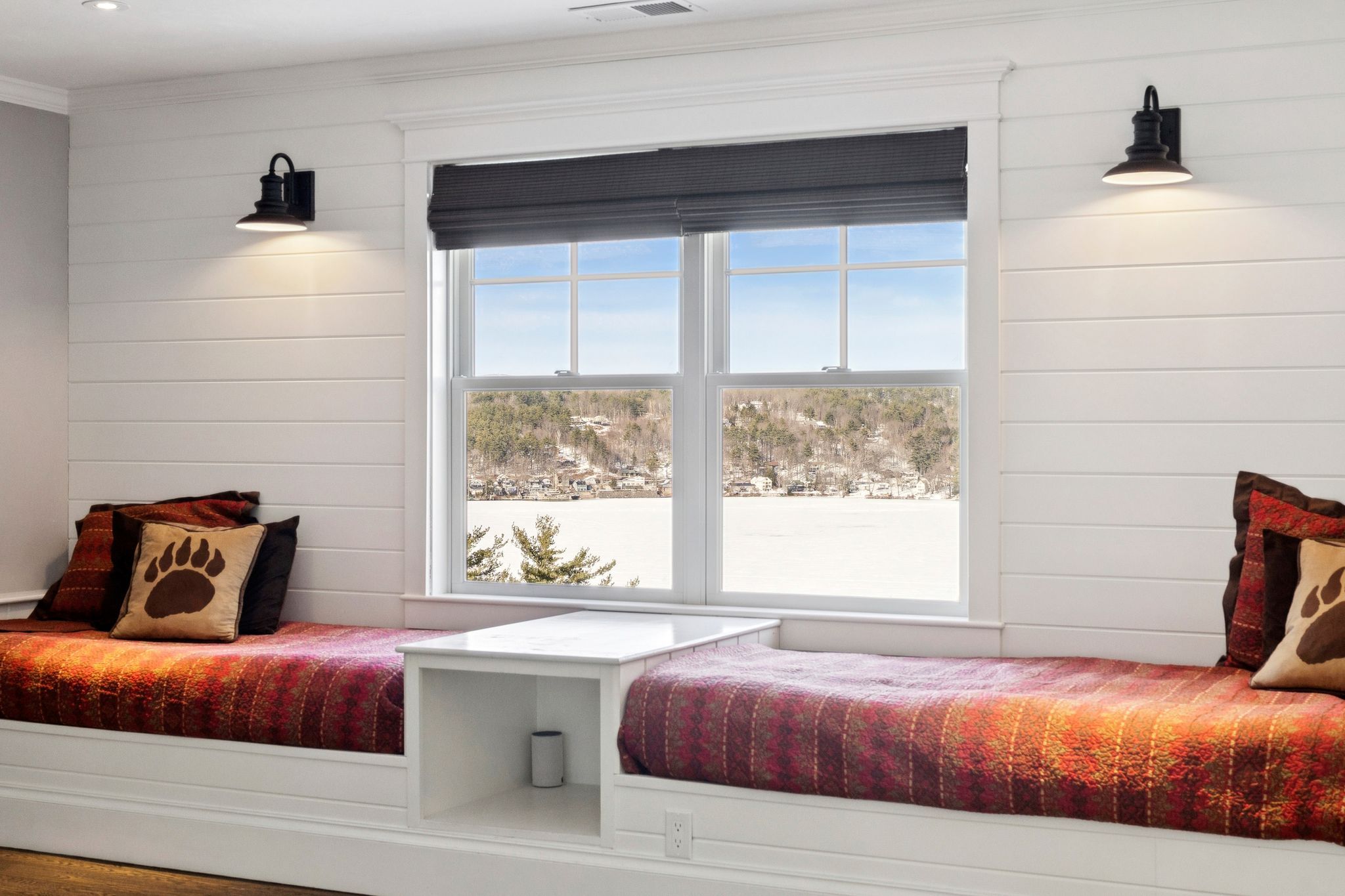 Bright bedroom with large arched window overlooking a green outdoor landscape, featuring a bed with cream-colored bedding, a wooden dresser with a vase of flowers, and a decorative mirror on a gray wall.