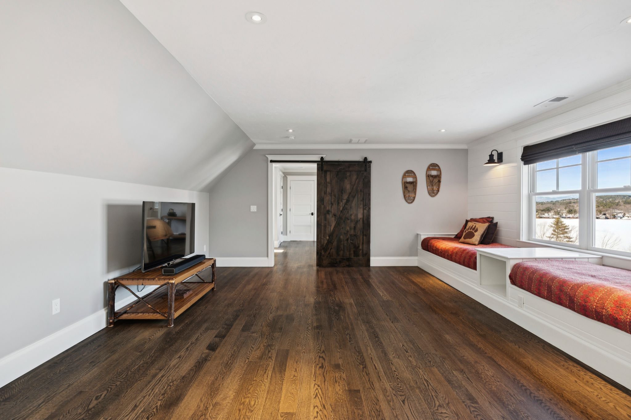 Bright bedroom with large arched window overlooking green trees, featuring a cozy bed with striped pillows, a wooden dresser with mirror, and contemporary decor.