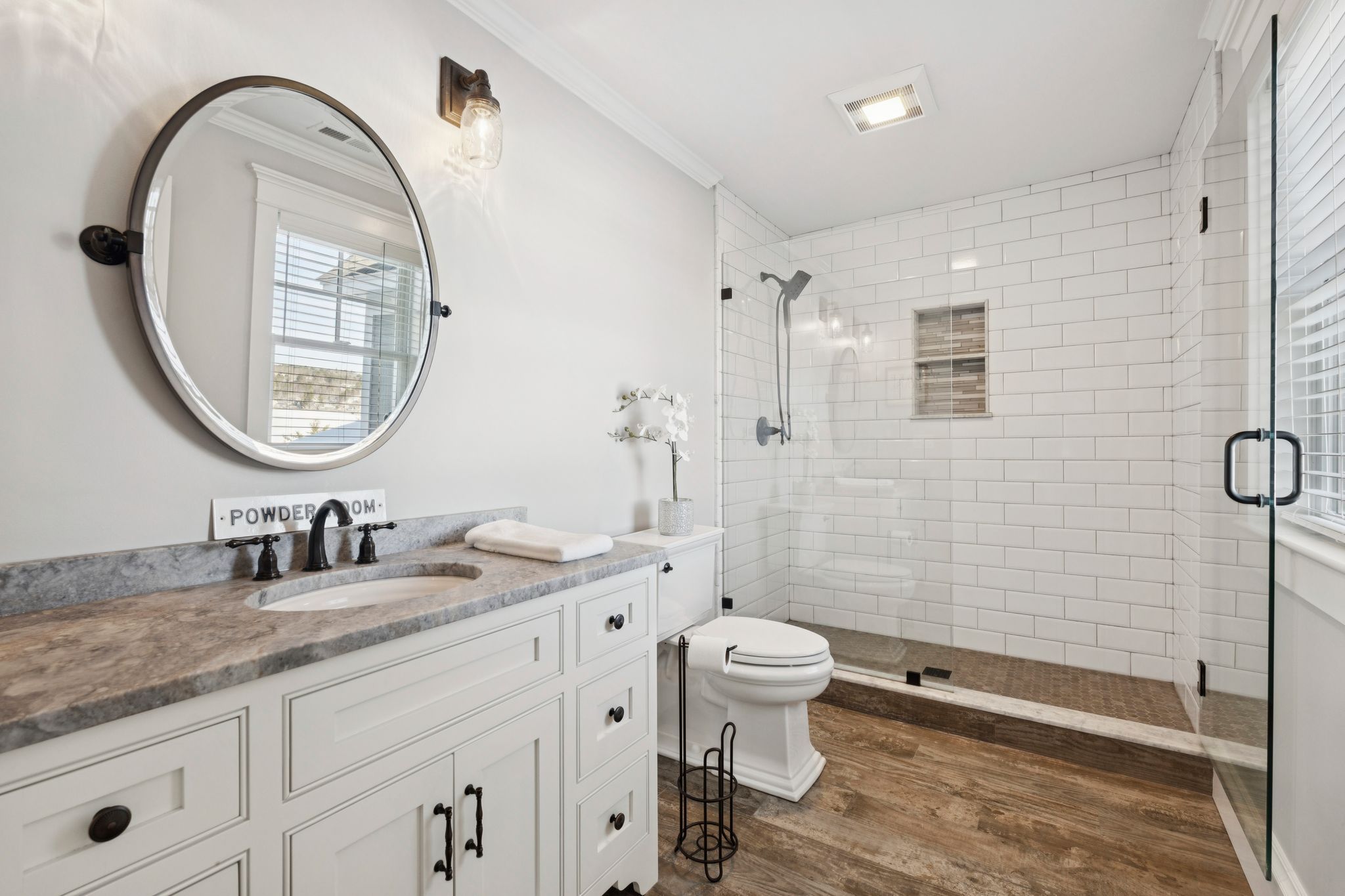 Modern bathroom interior with double sink vanity, granite countertop, decorative plants, soap dispensers, towels, and a toilet, featuring neutral wall colors and a large mirror.