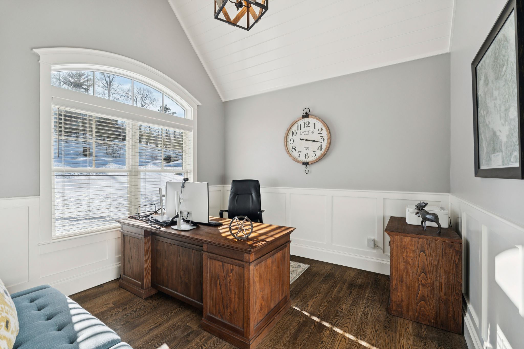 Spacious basement game room with shuffleboard, pool table, and seating area, featuring large windows and hardwood floors.