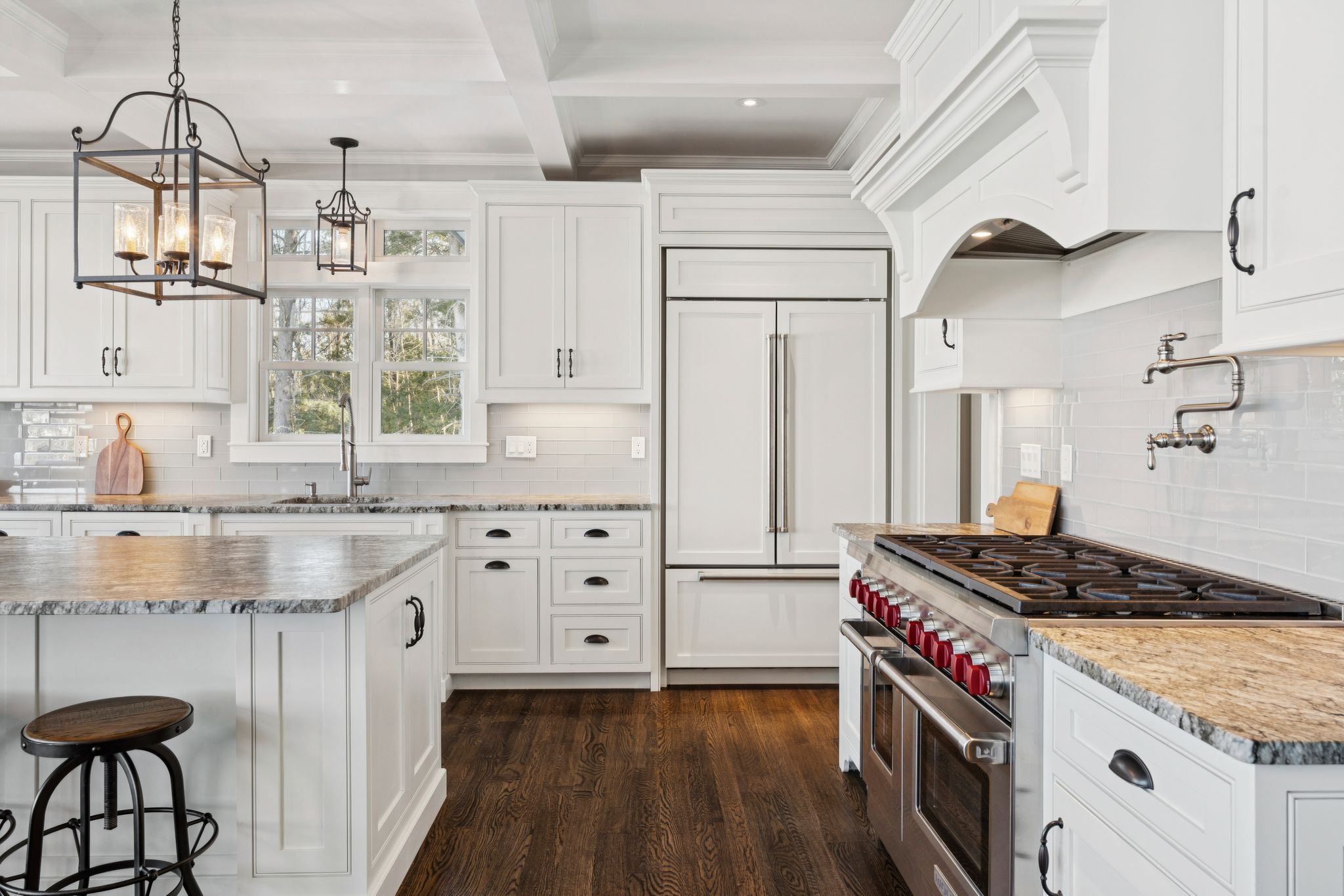Modern kitchen with granite countertops, grey cabinetry, mosaic backsplash, stainless steel appliances, and a breakfast bar with blue upholstered chairs, featuring a dining area with a vase of yellow flowers and ocean-themed artwork on the wall.