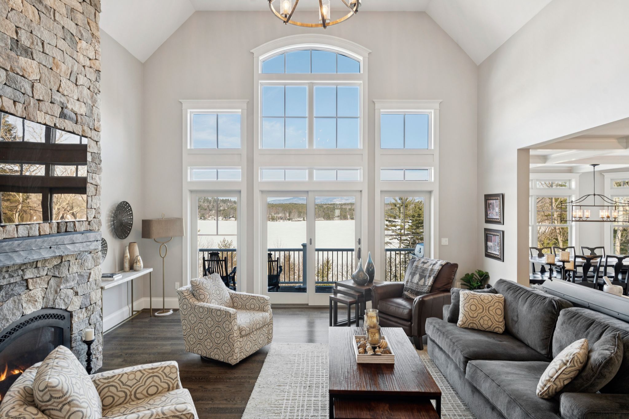Modern kitchen with granite countertop, farmhouse sink, stainless steel faucet, and view of bright living room with large windows and greenery.