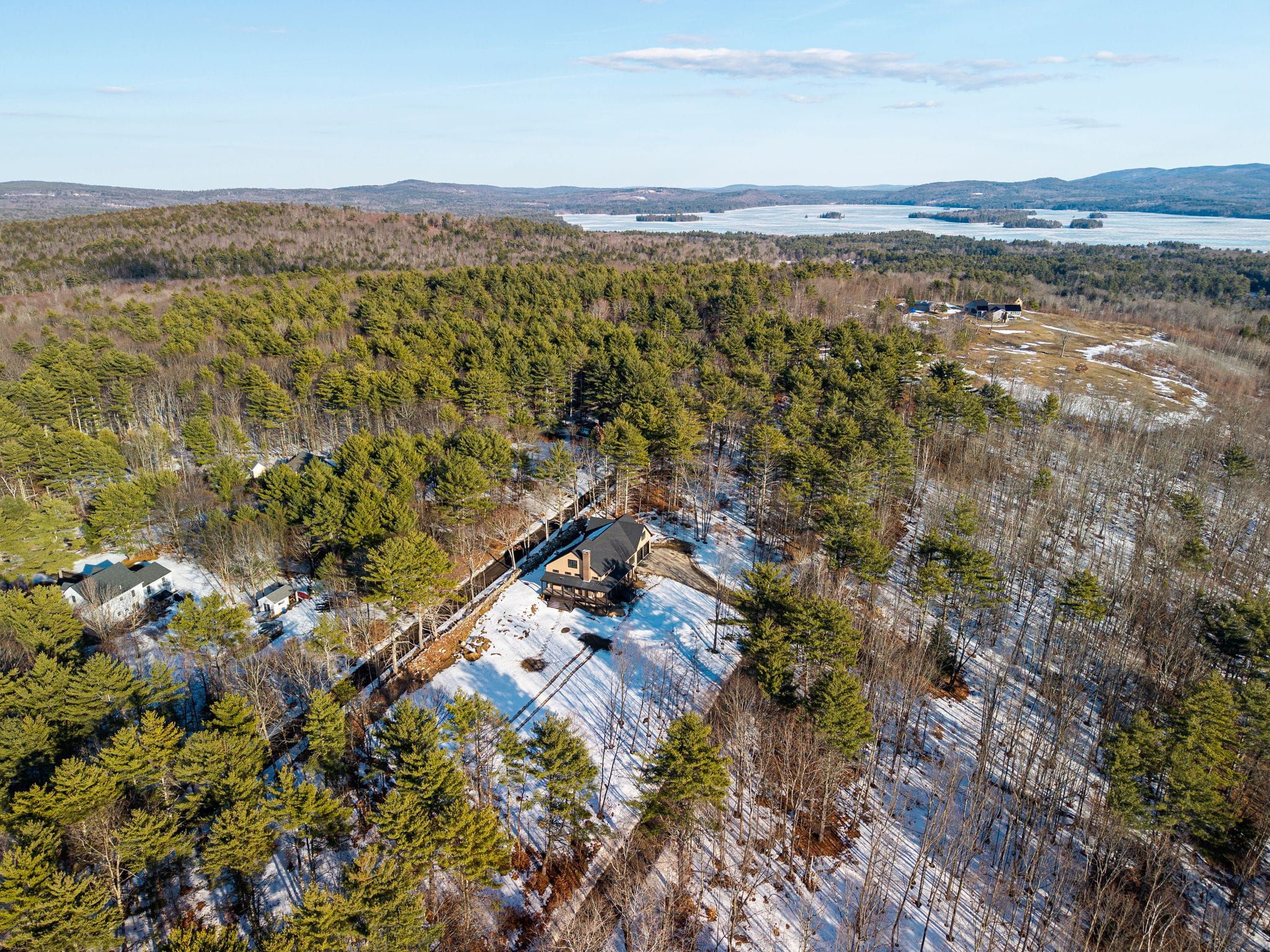Spacious green modern house with multiple decks and large windows, located in a snowy landscape surrounded by trees.