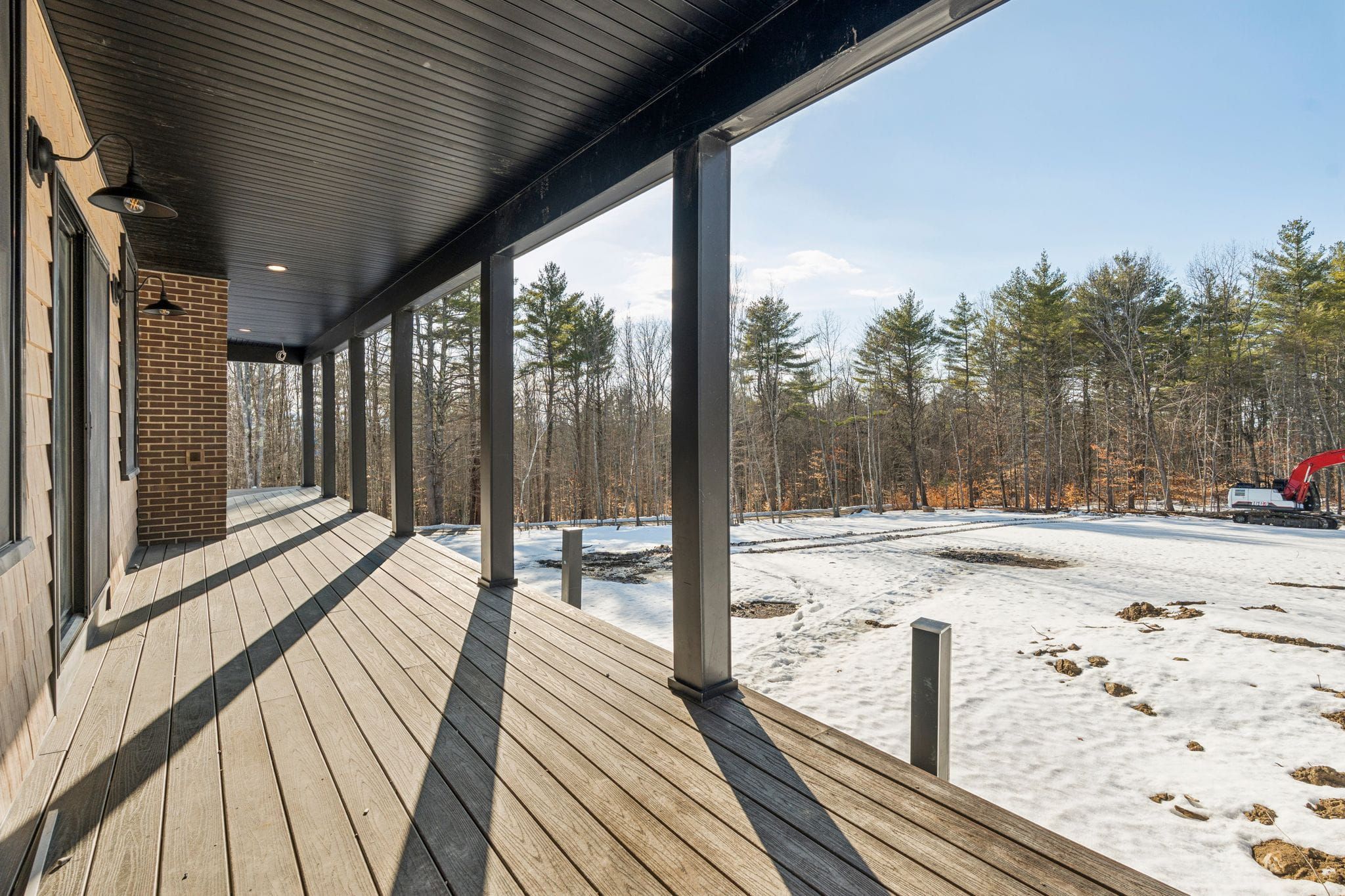 Spacious green residential house with snow-covered yard and trees on a bright winter day