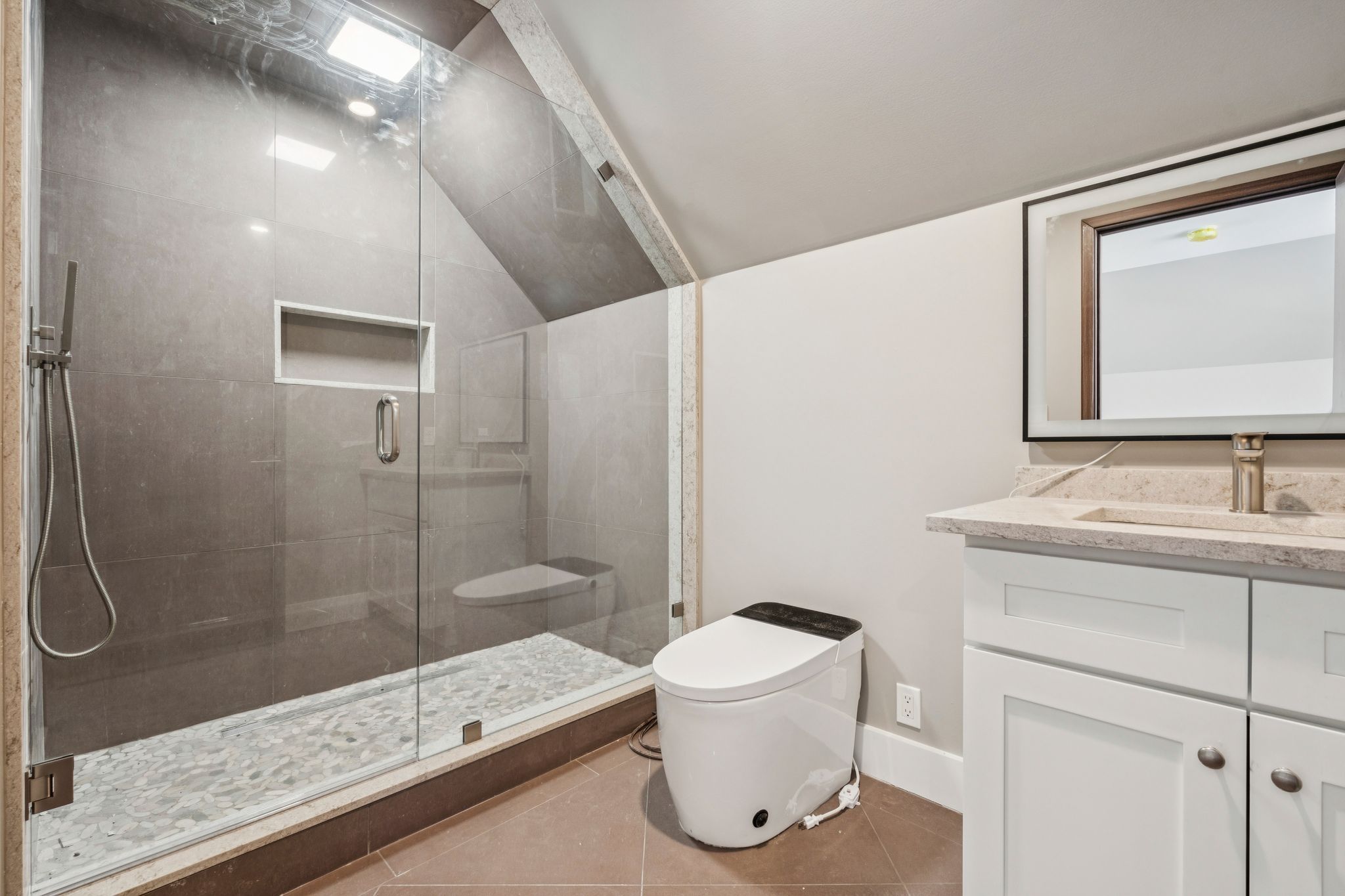 Living room with built-in white shelving unit, large flat-screen TV, leather recliner, side table with lamp, and window with patterned valance.