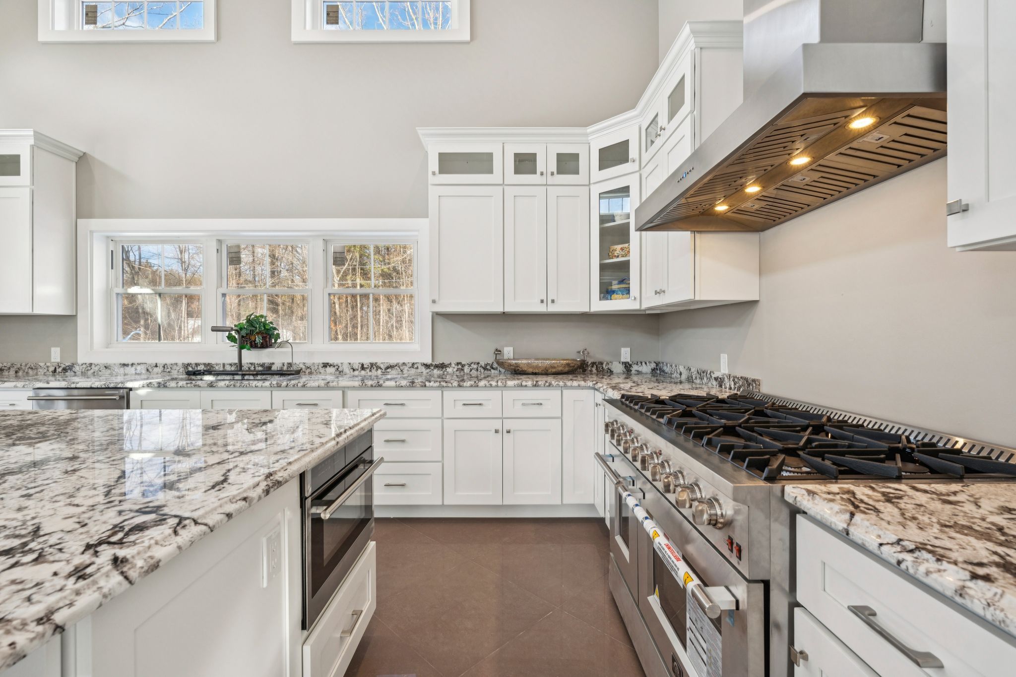 Modern kitchen with white cabinetry, granite countertops, and a central island with four wooden barstools, featuring pendant lighting and a sliding glass door leading to an outdoor patio.