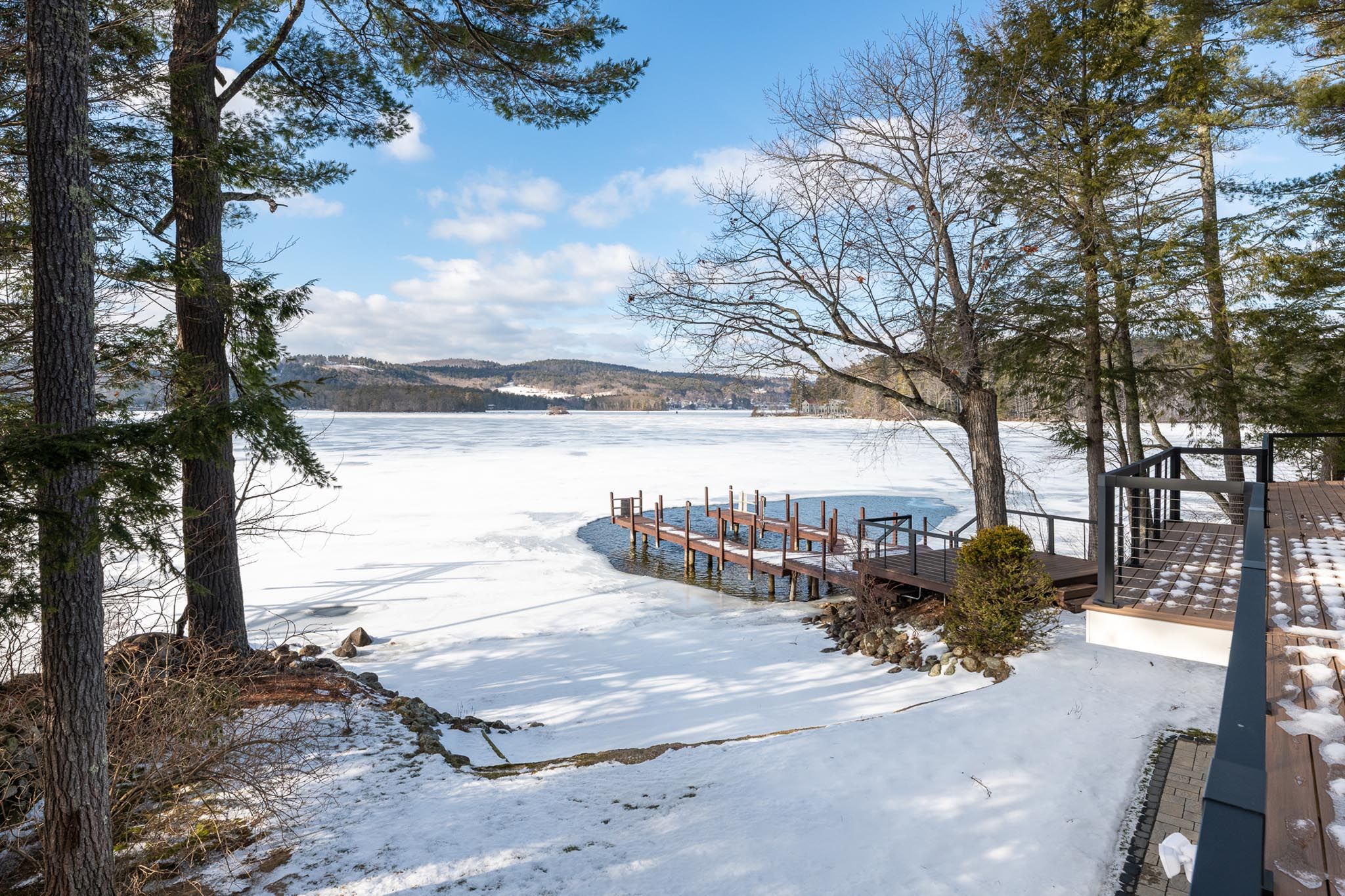 Modern house exterior with dark gray siding, stone front steps, wooden front door with glass panels, surrounded by landscaped garden with small trees and plants, in a suburban neighborhood