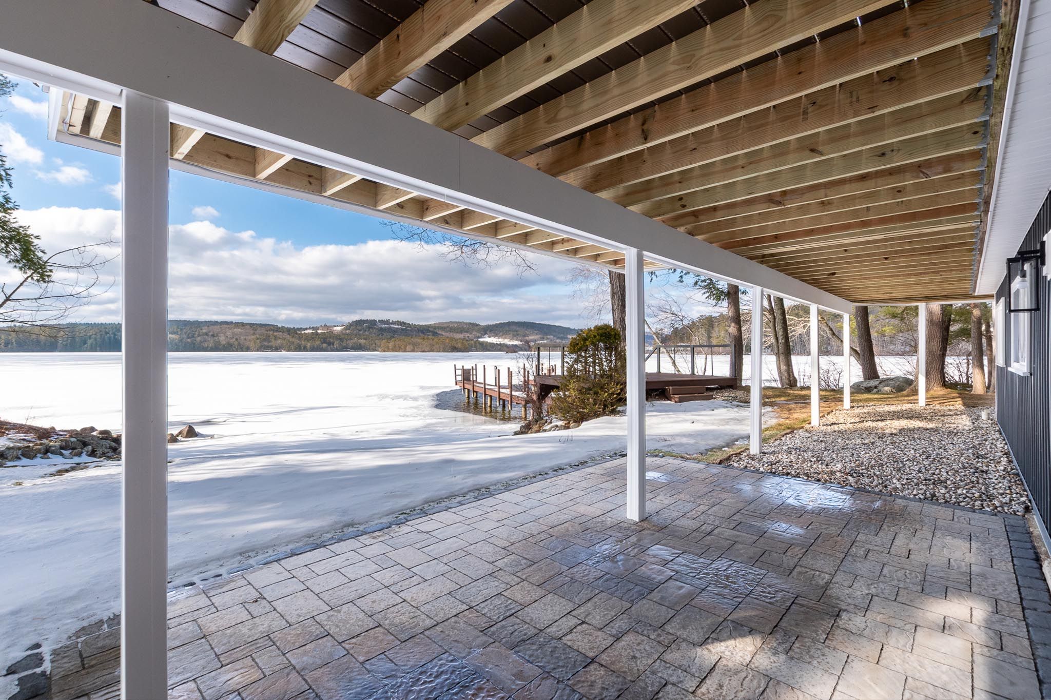 Modern residential house with a detached garage featuring a wooden door, surrounded by trees and landscaped yard with gravel accents.