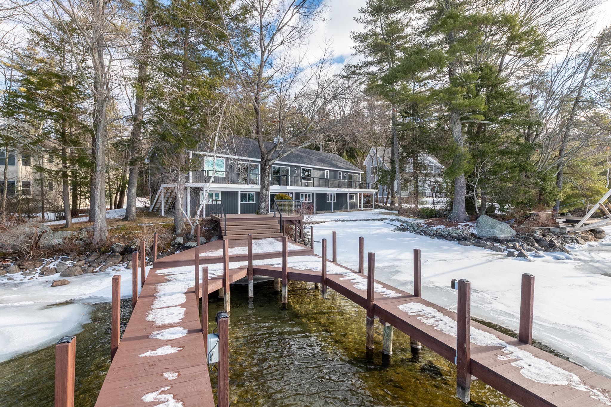 Modern blue house with landscaped front yard, stone steps, and surrounding trees in a suburban neighborhood