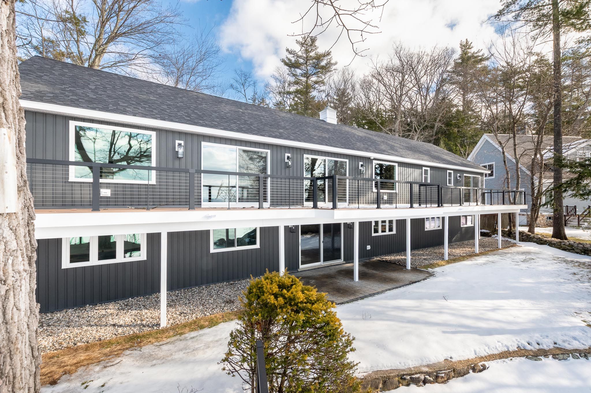 Modern black two-story house with illuminated windows and front steps at dusk, surrounded by trees and landscaped yard