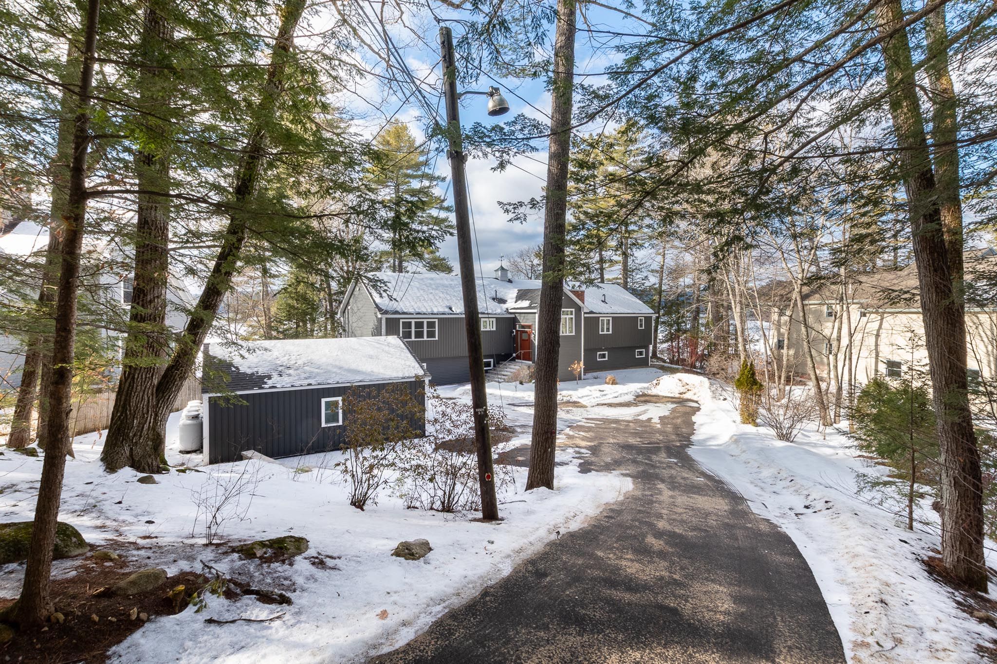 Aerial view of a lakeside home surrounded by trees, featuring a wooden dock, a boatslip with a boat, and a small sandy area with a blue kayak.