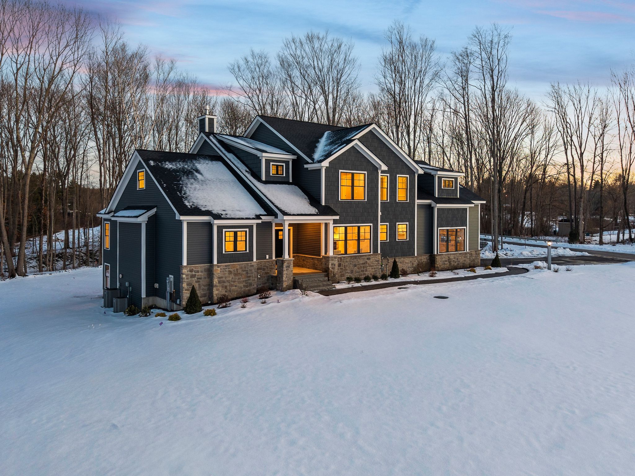 Modern black house with a stone foundation and snow-covered landscape during sunset