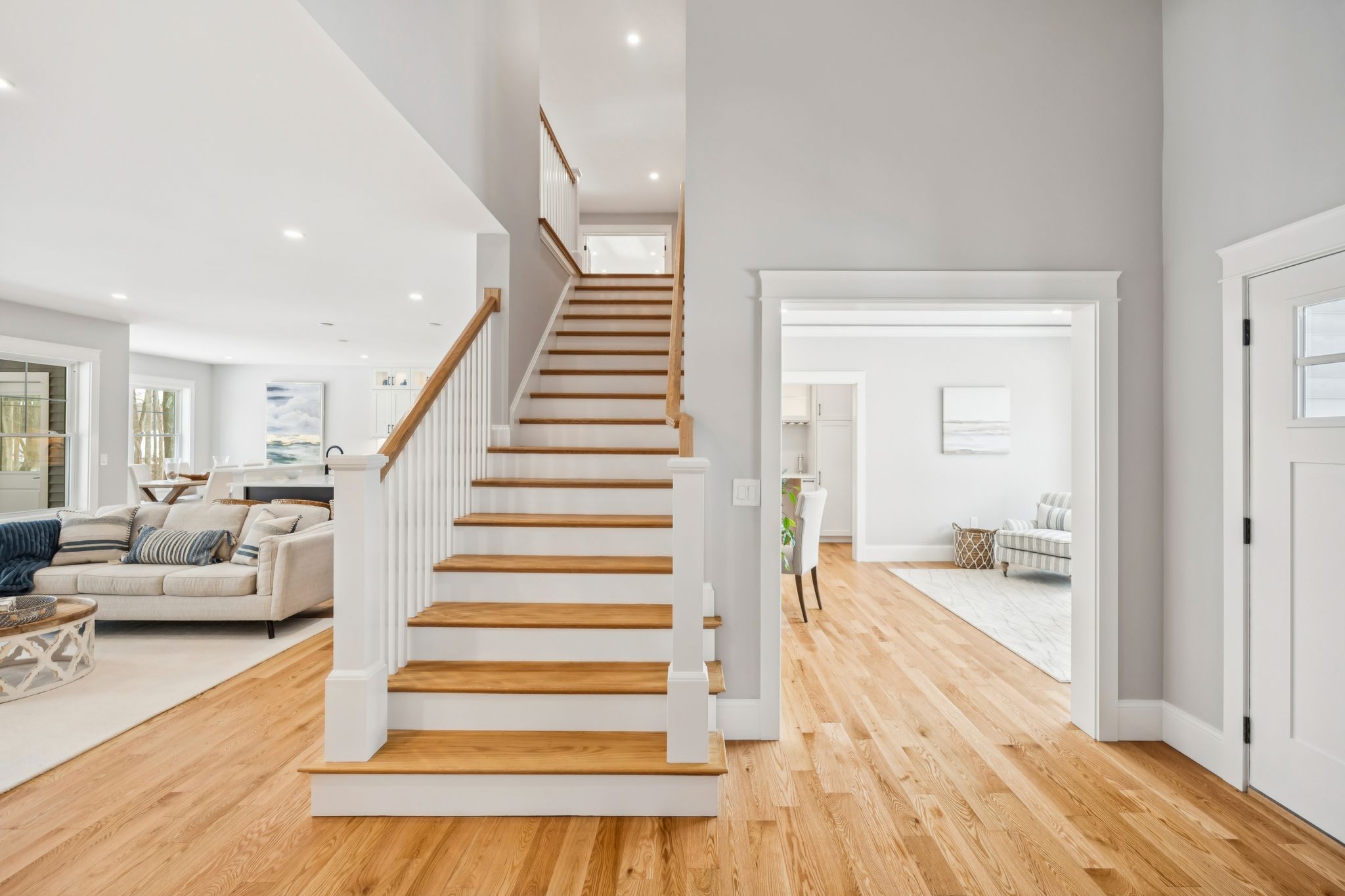 Bright and airy modern home interior with wooden staircase, white walls and trim, open living and dining areas, natural light, contemporary furniture, and hardwood flooring.