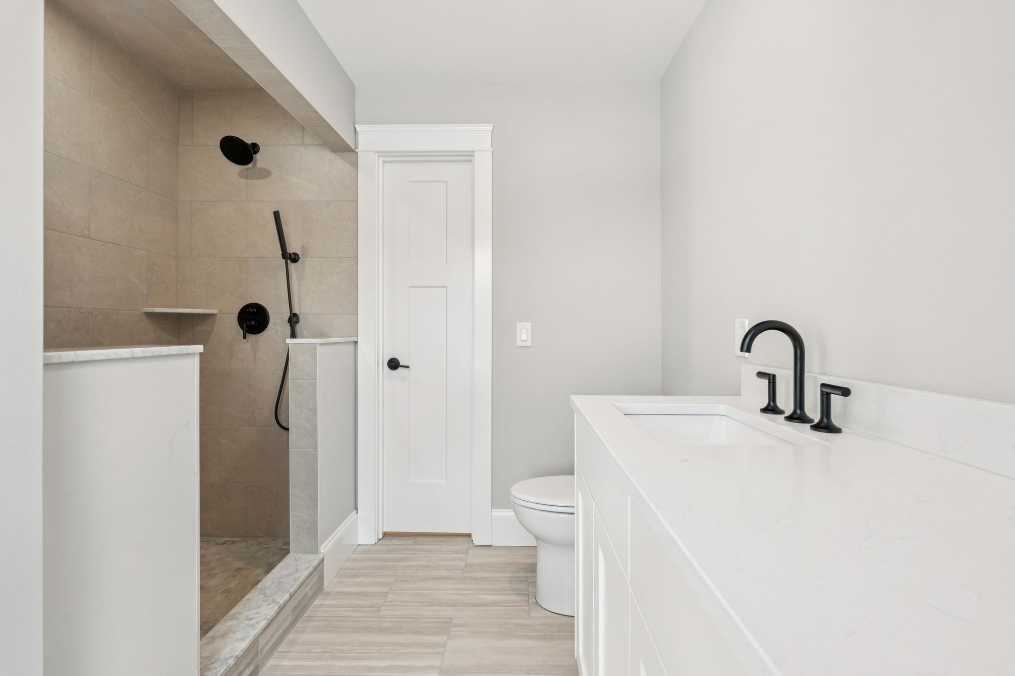 Modern minimalist bathroom with walk-in shower, white vanity with black fixtures, and light wood flooring