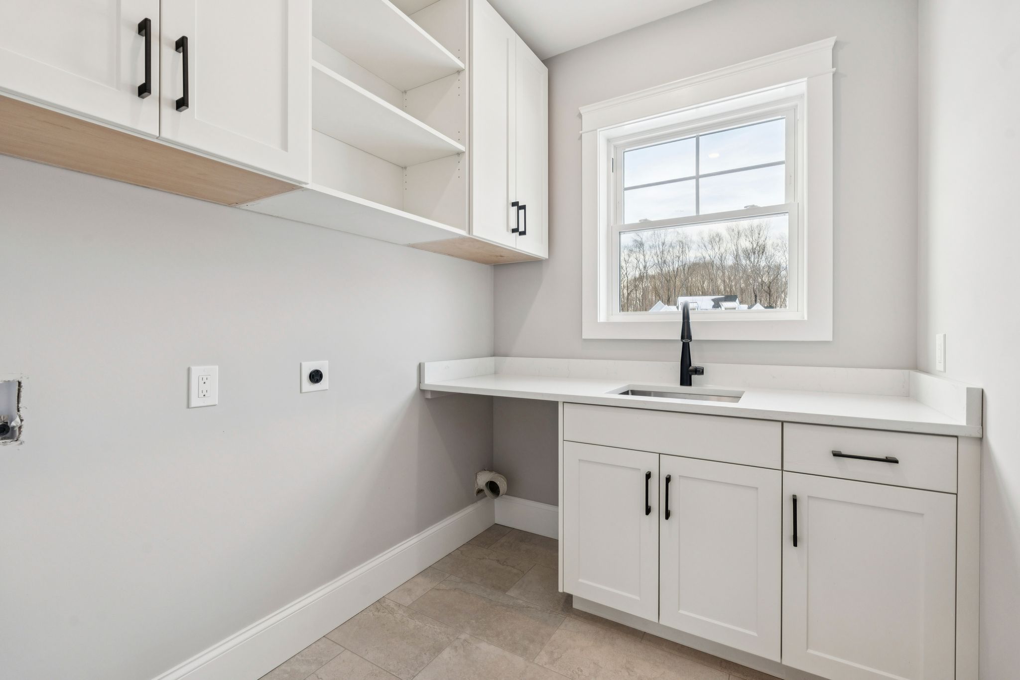 Modern laundry room with white cabinetry, black hardware, a black faucet, and a large window providing natural light.
