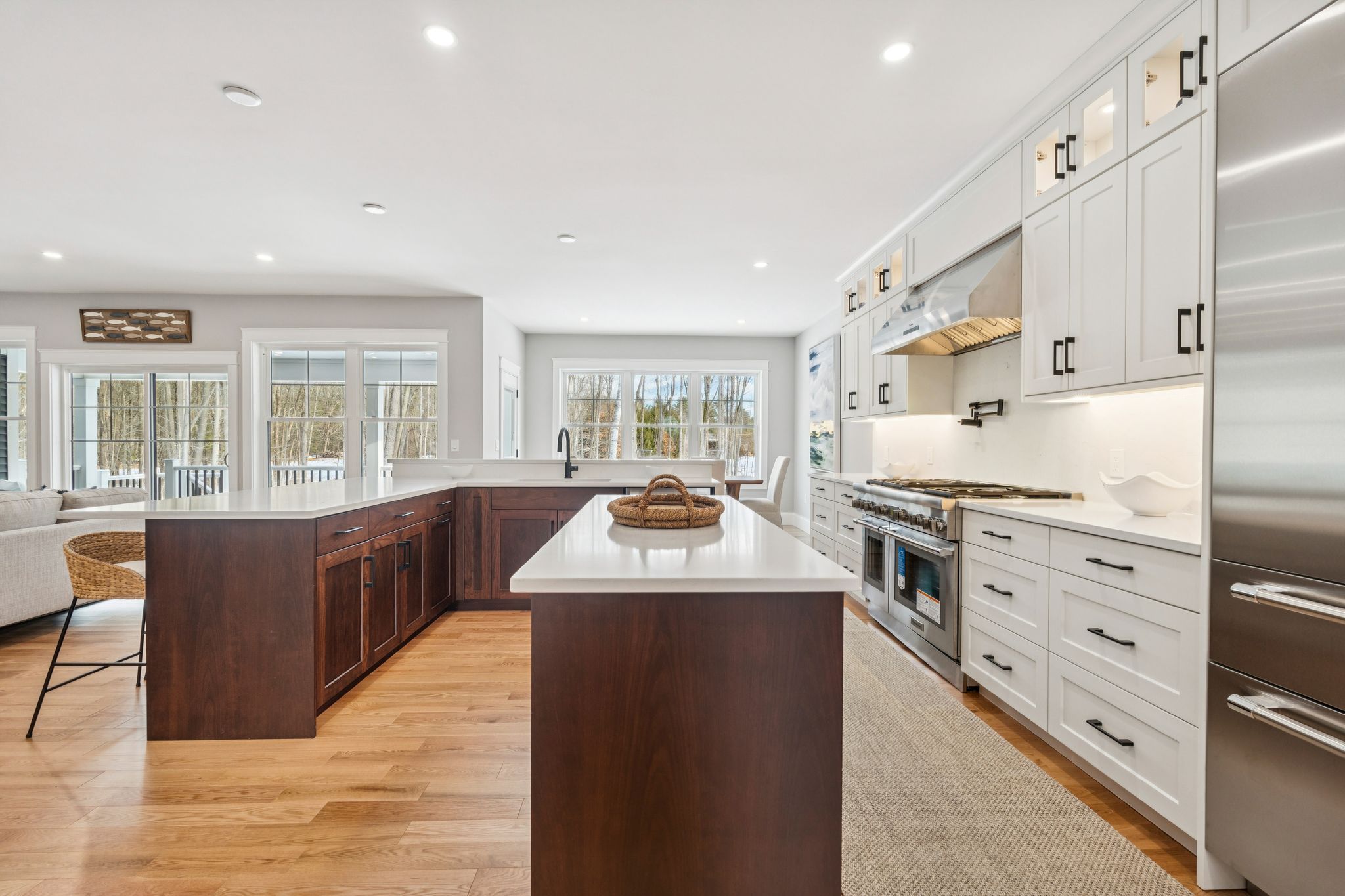 Modern kitchen with white cabinetry, stainless steel appliances, a large central island with dark wood finish, and natural light from multiple windows overlooking an outdoor view with trees.
