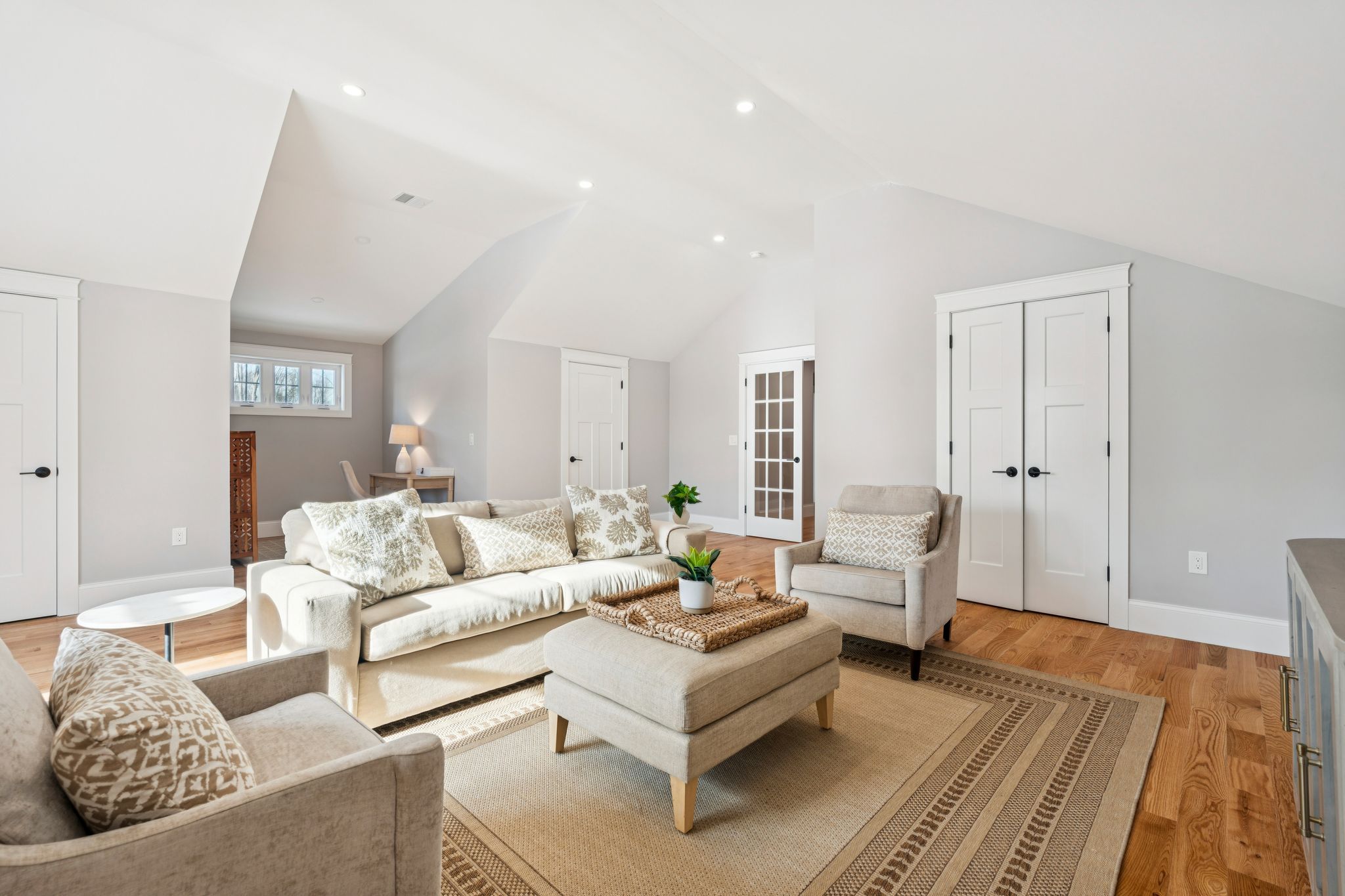 Bright and modern living room with white sofa, beige armchairs, wooden flooring, and natural light in a contemporary home interior
