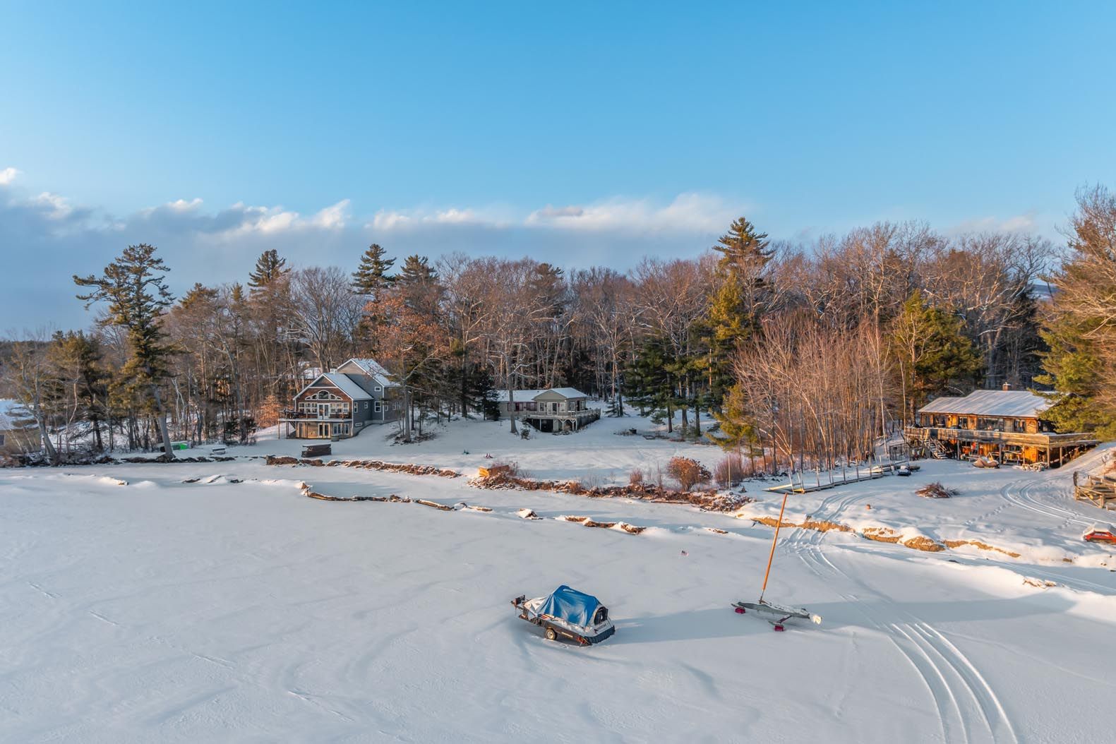 Aerial view of a lakeside property with a house nestled among trees, a well-maintained lawn, a dock on the lake, and mountainous backdrop in a scenic, lush green setting.