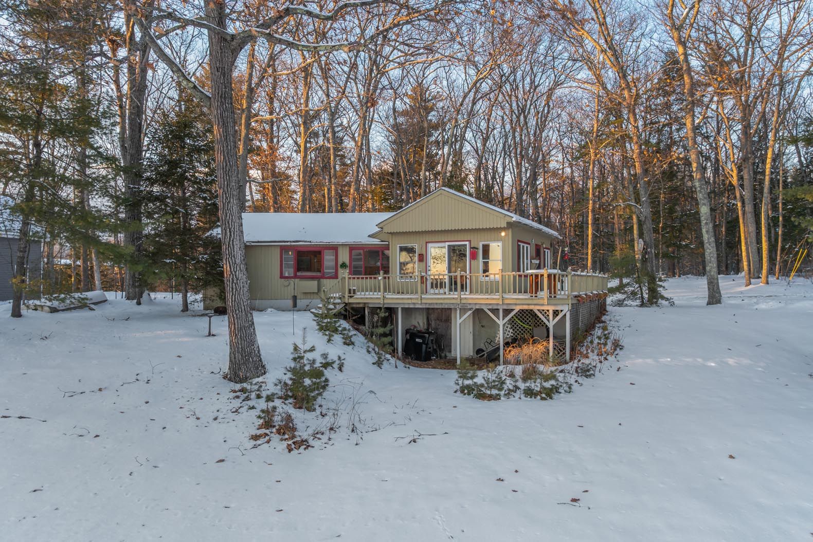 Aerial view of a peaceful lakeside property with multiple docks, boats, a house surrounded by lush green trees, and rolling mountains in the background during daytime.