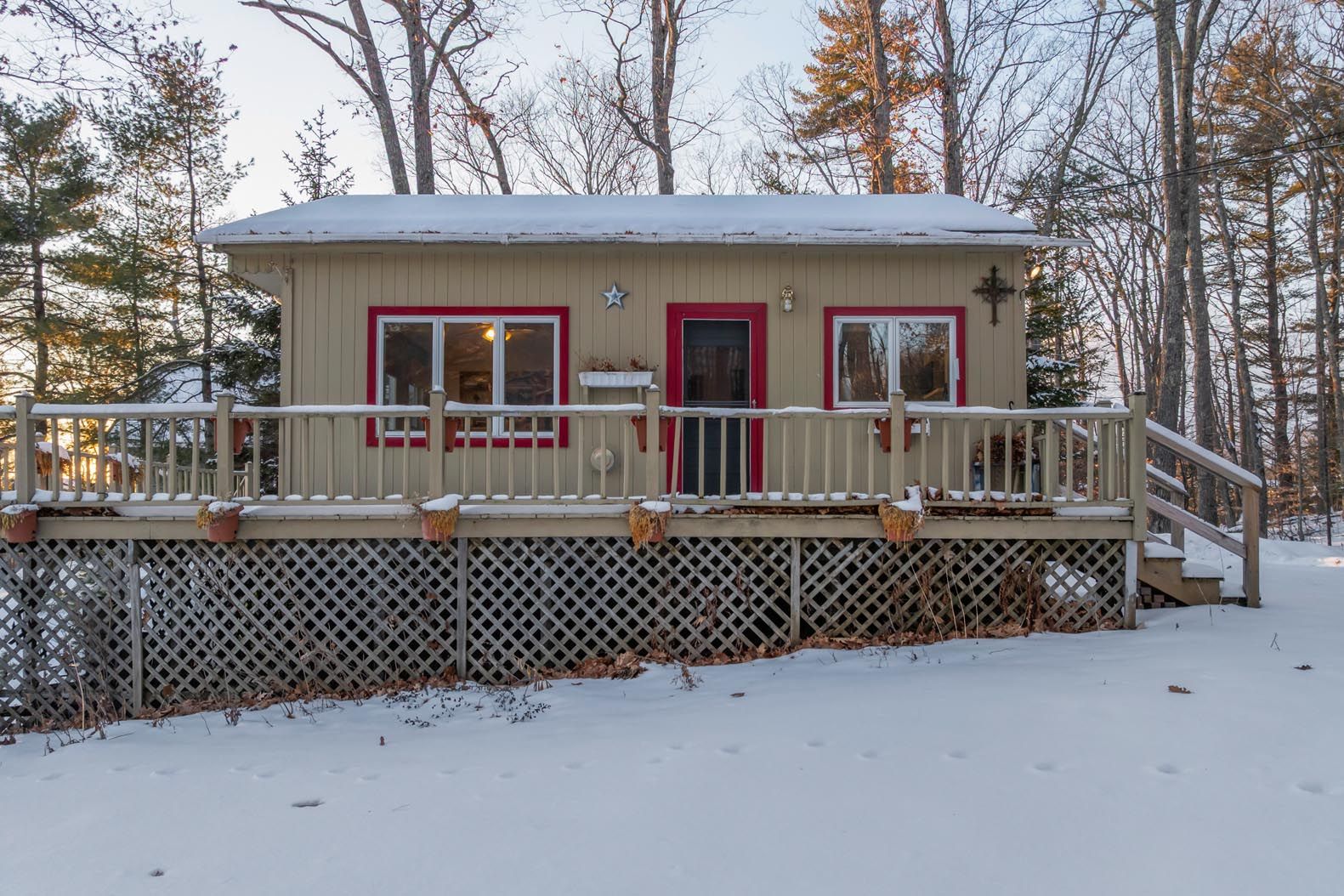 Scenic lakeside view with houses, dock, and boats surrounded by lush green trees and forested mountains in the background